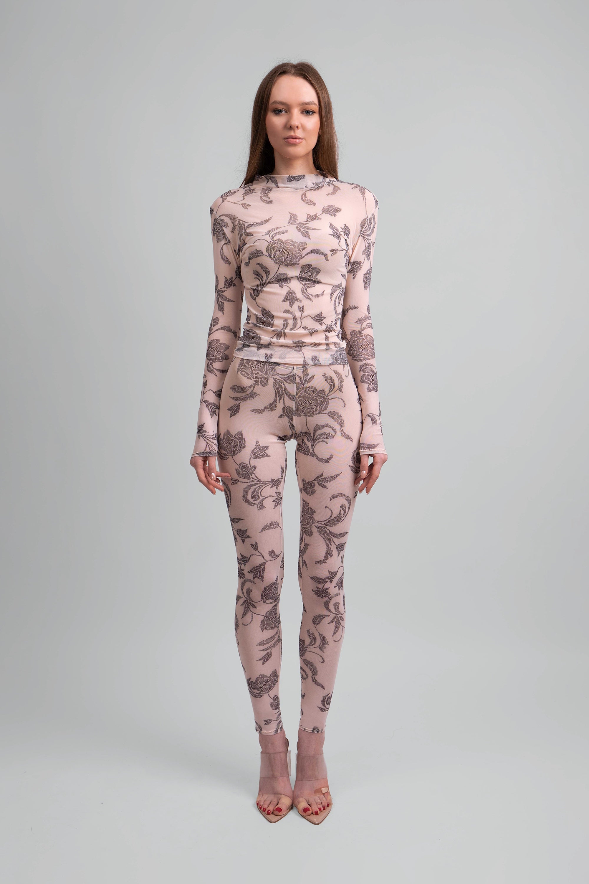 Woman wearing a sheer pink and grey floral patterned top and leggings on a plain background