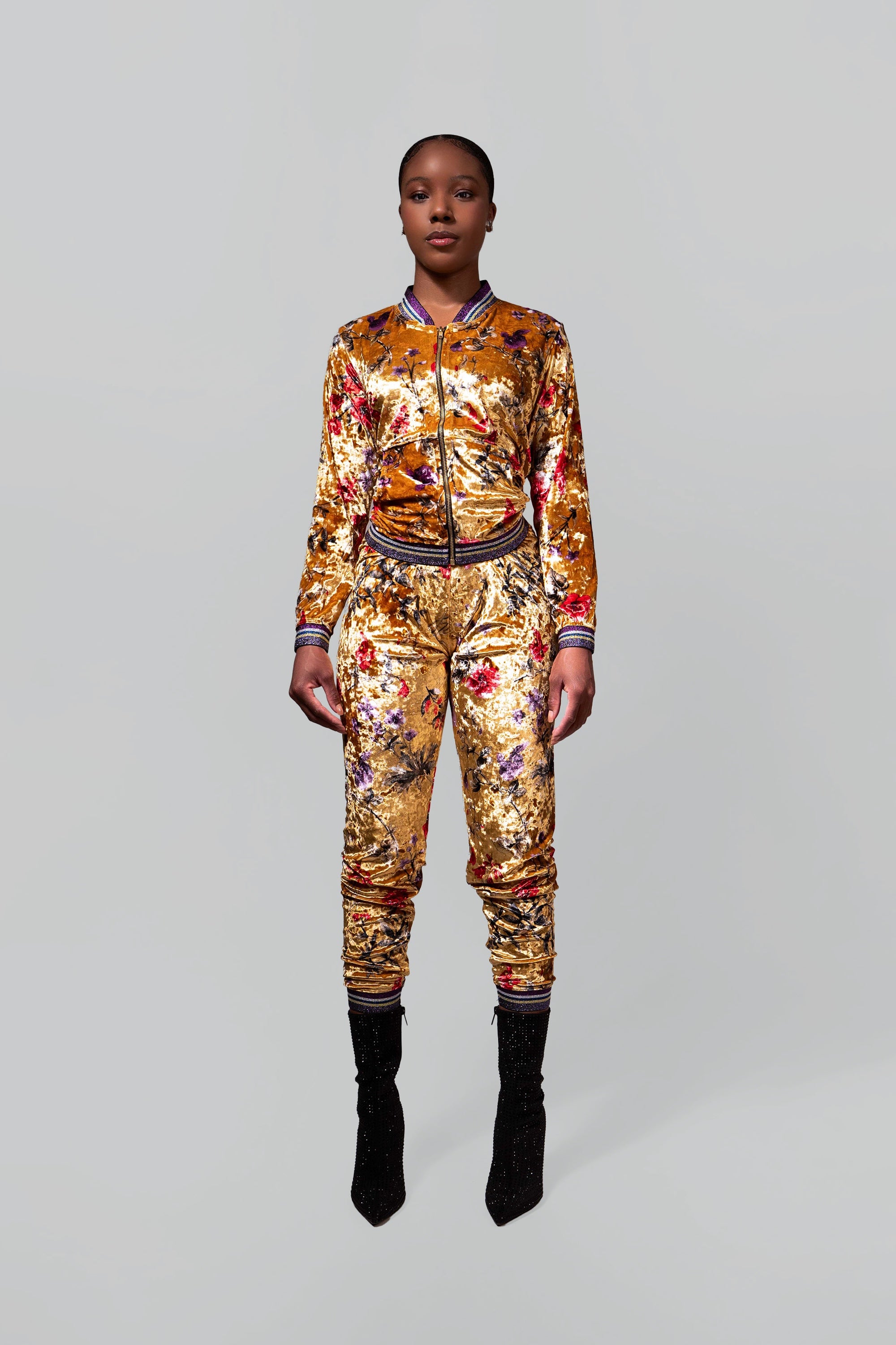 Woman wearing a gold velour tracksuit with red and purple floral accents