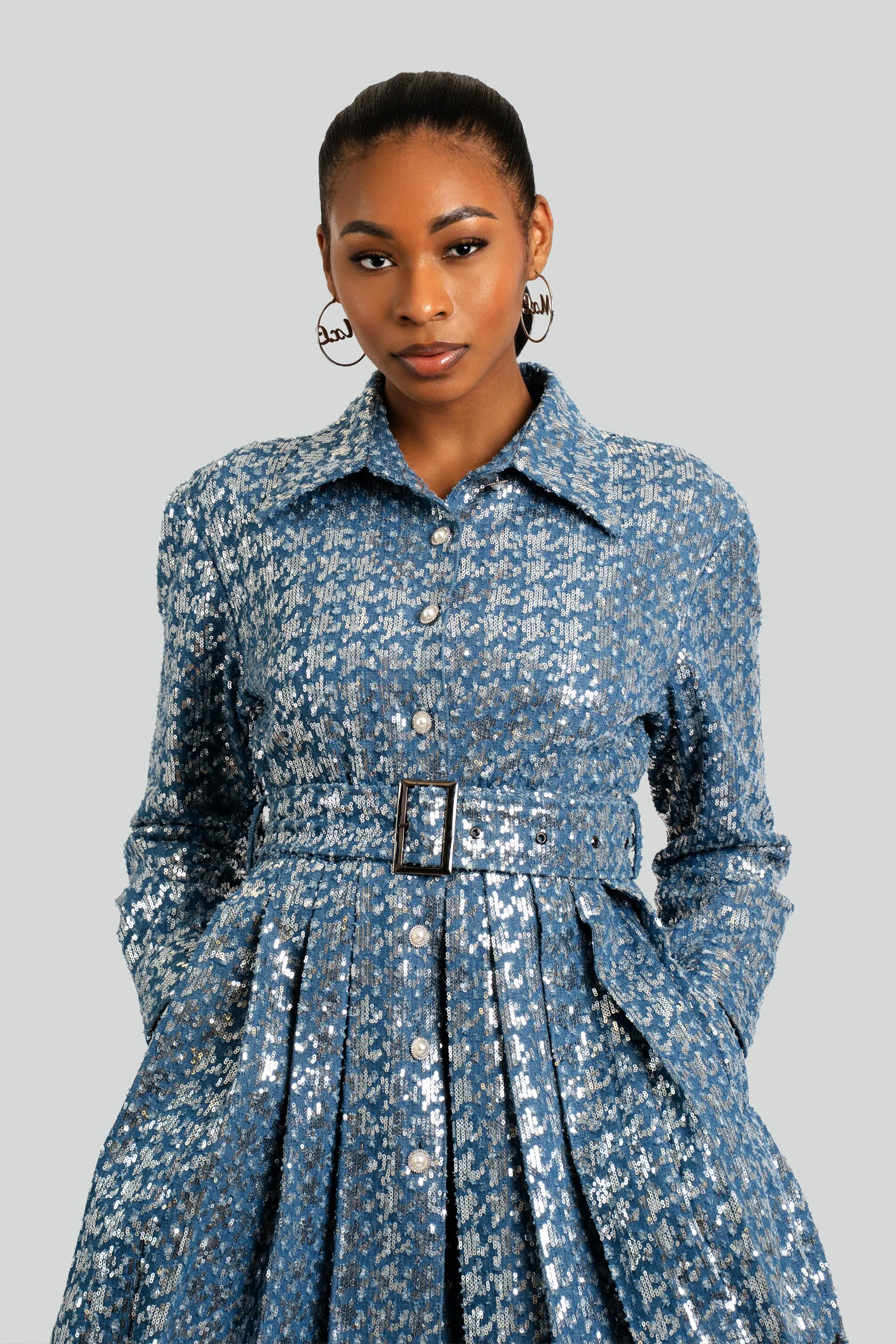 Model styling a blue sequined designer dress with a tailored bodice, waist belt, and pleated flare skirt