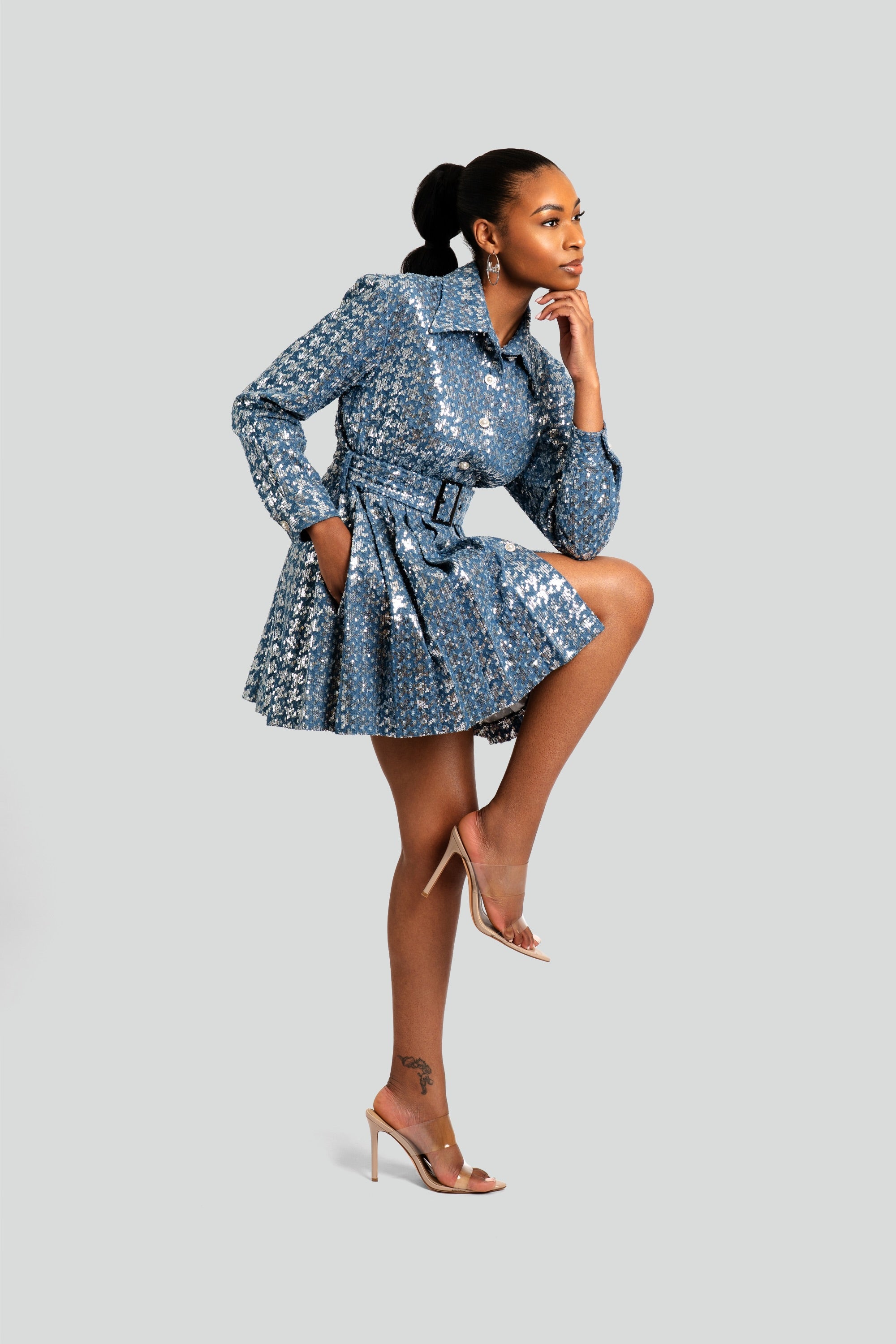Woman wearing a structured blue sequin mini dress with a matching belt, sharp collar, and a modern pleated silhouette by Maui X Lolita