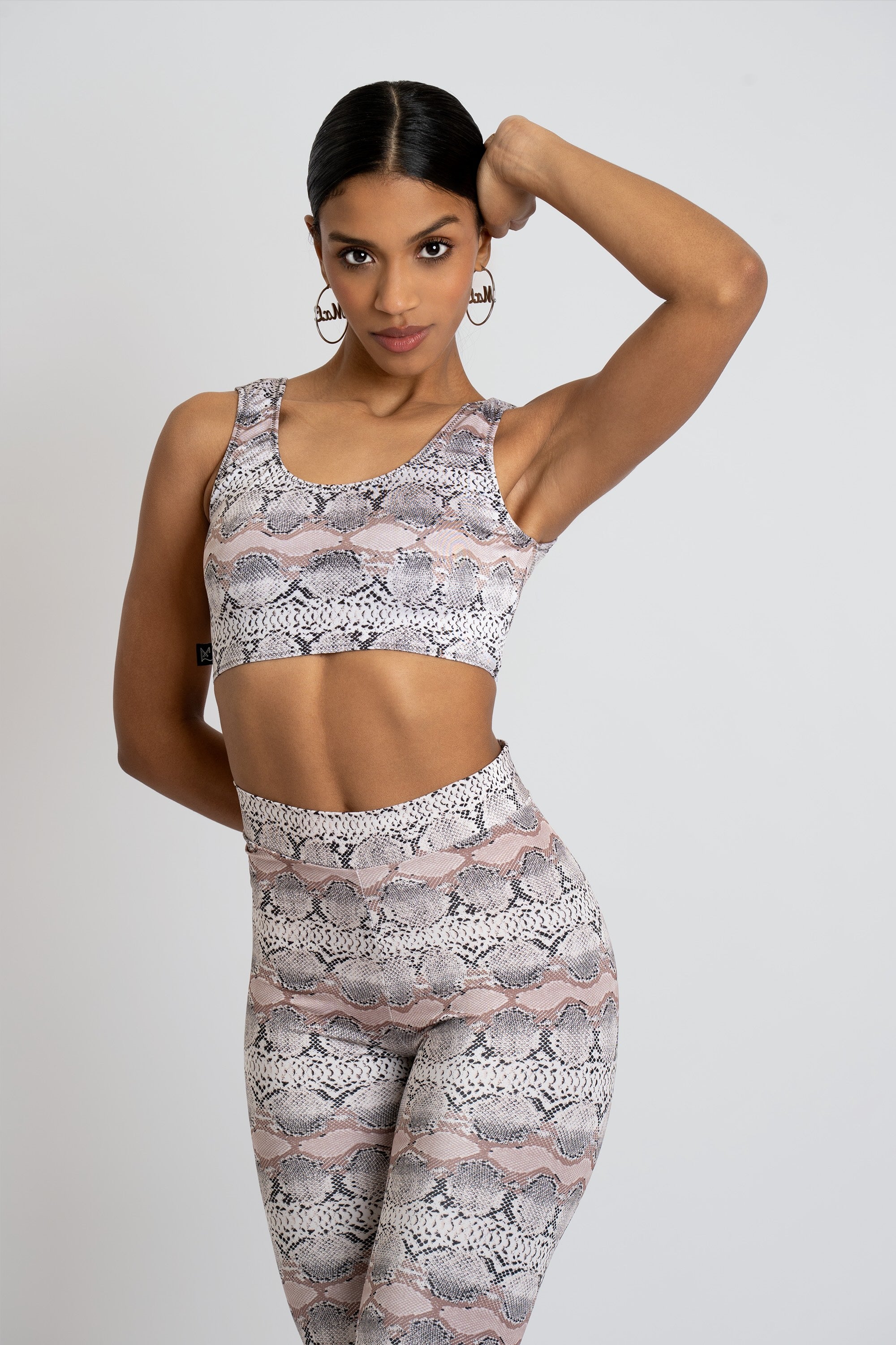 Woman wearing a matching snakeskin print sports bra and leggings set on a white background