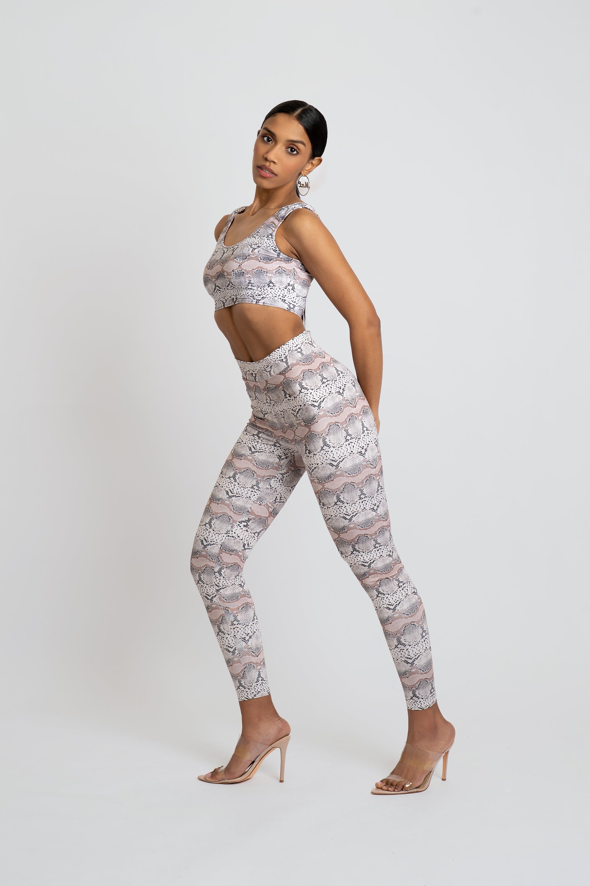 Woman wearing a matching snakeskin print sports bra and leggings set on a white background
