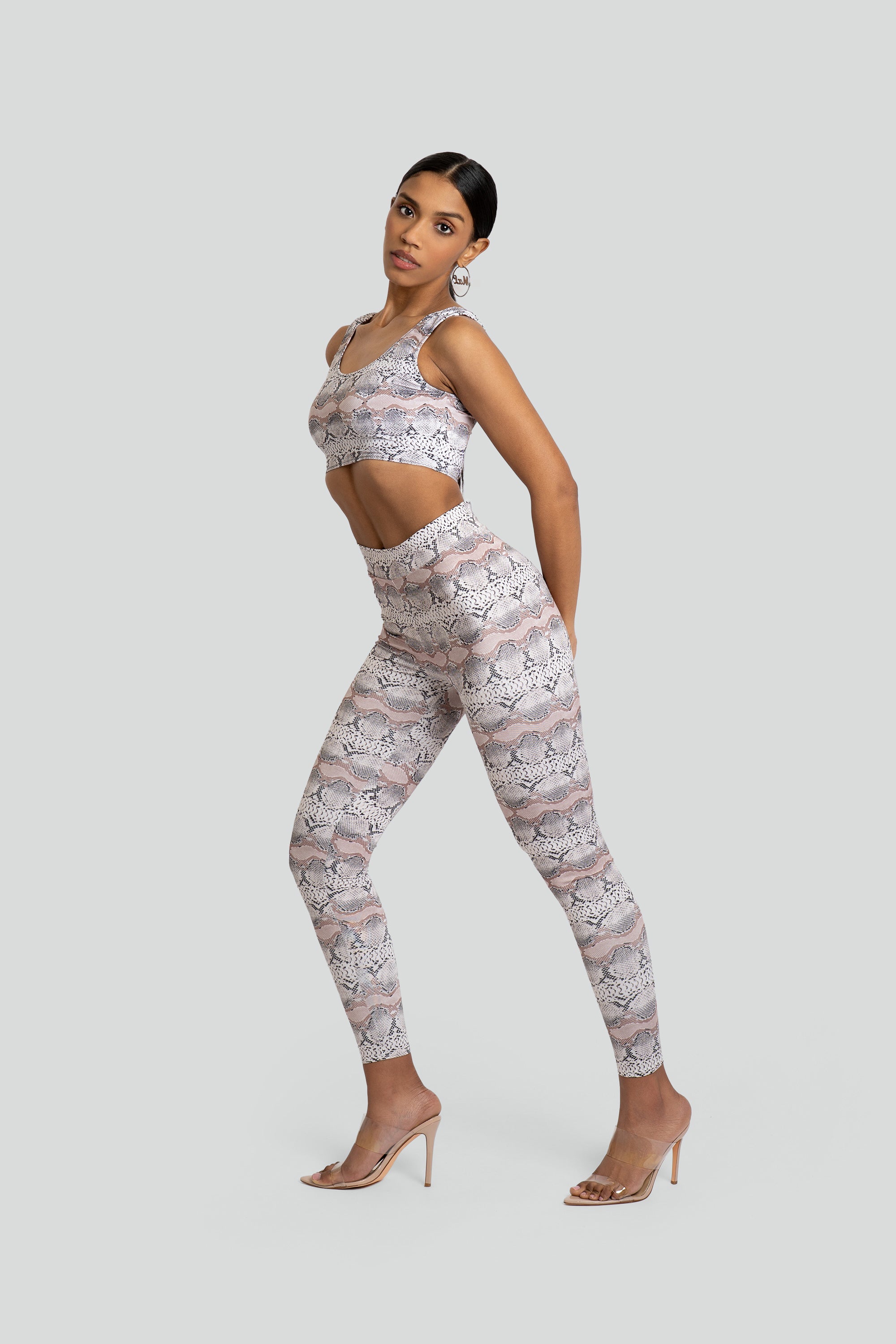 Woman wearing a matching snakeskin print sports bra and leggings set on a white background
