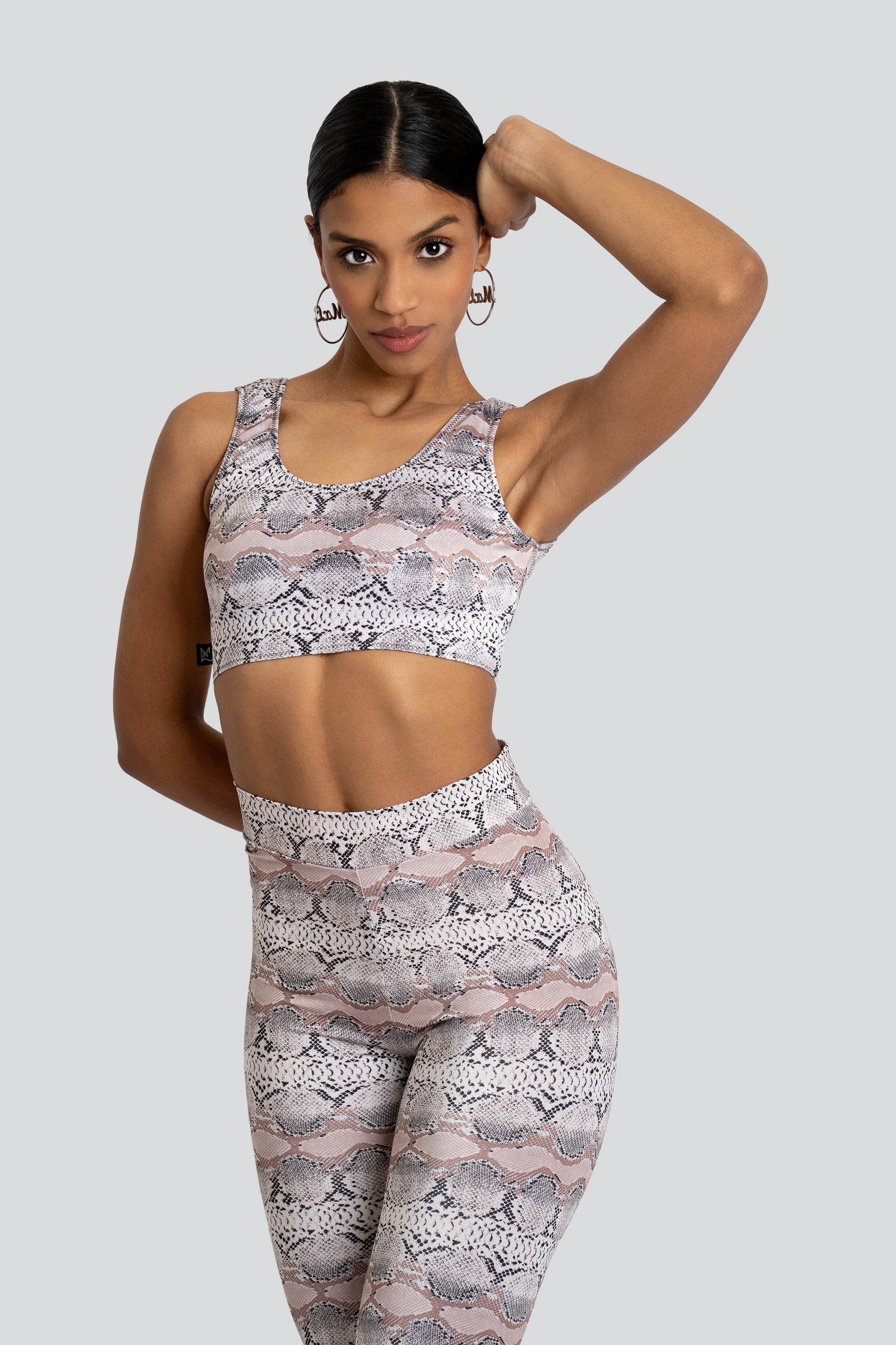 Woman wearing a matching snakeskin print sports bra and leggings set on a white background