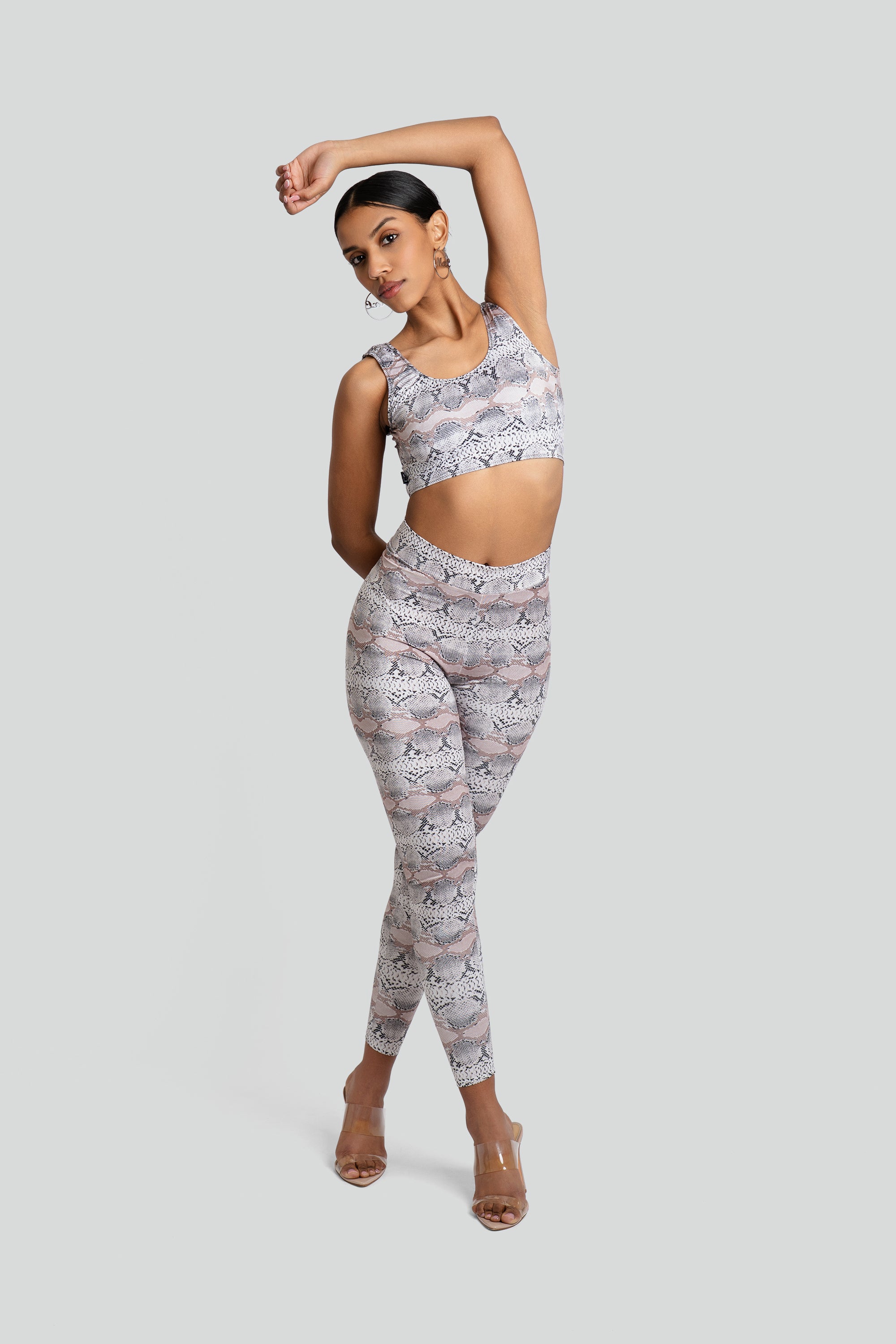 Model wearing a neutral snakeskin-print workout two-piece set featuring a sleeveless crop top and matching high-waisted leggings