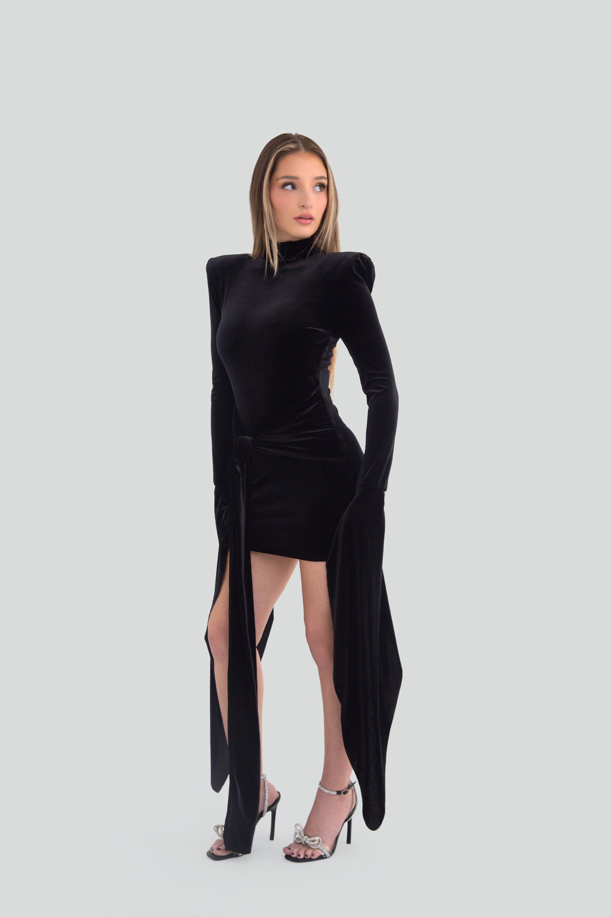 Woman wearing a black mini dress with dramatic long sleeves on a plain background