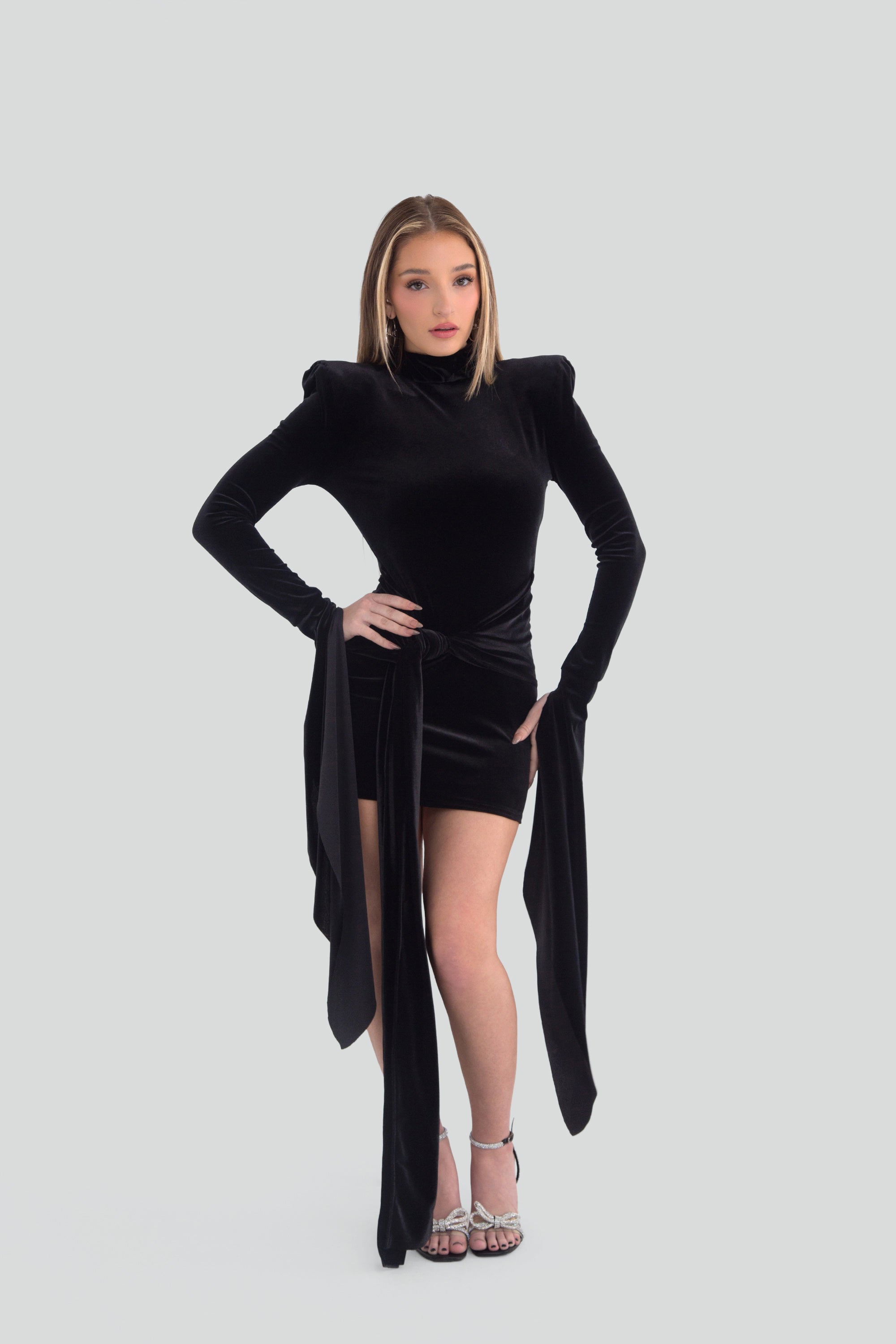 Woman wearing a black mini dress with dramatic long sleeves on a plain background