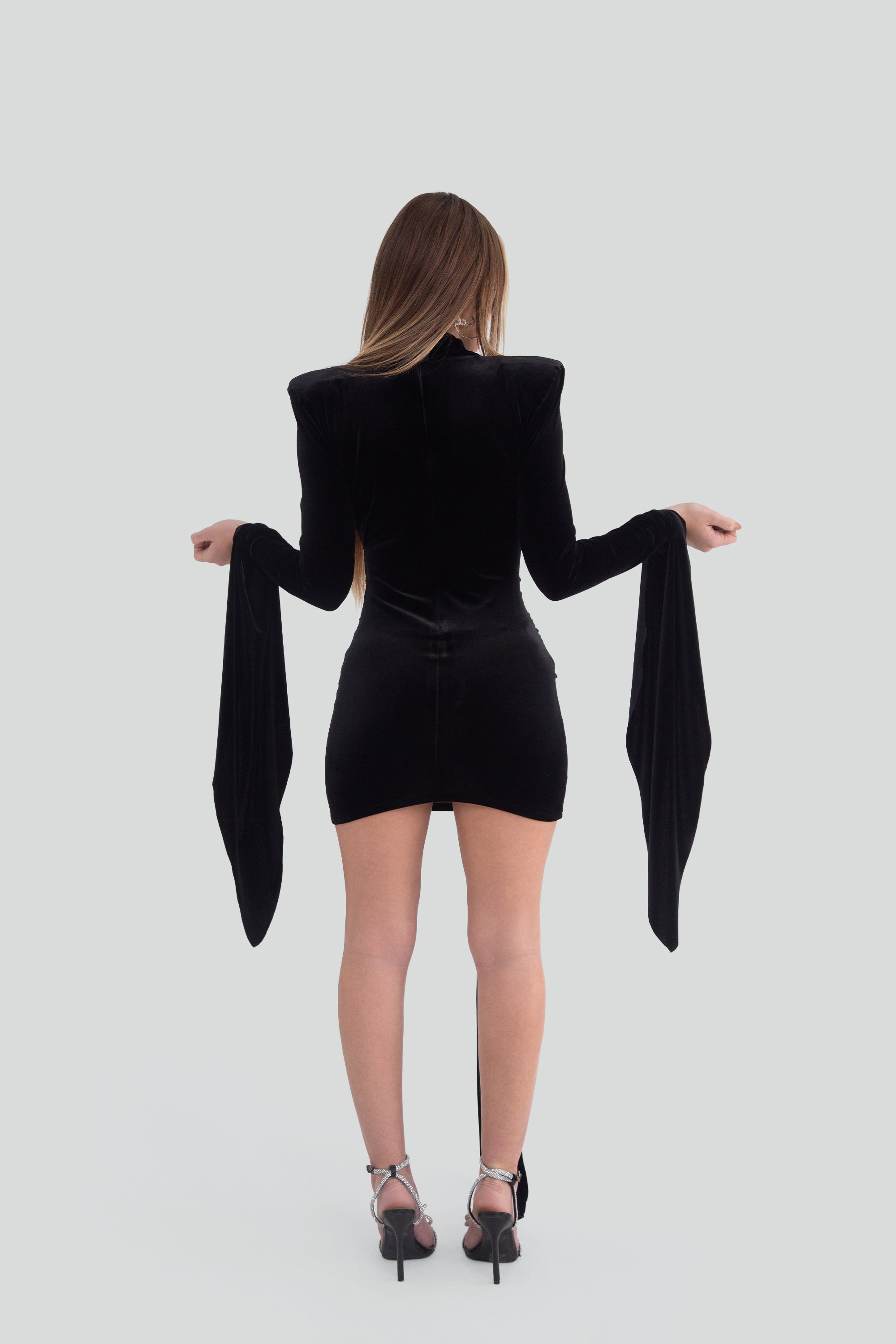 Woman wearing a black mini dress with dramatic long sleeves on a plain background