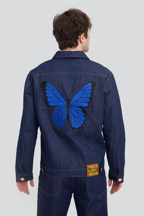 Back view of a man wearing an oversized blue denim jacket featuring a large intricate embroidered butterfly wing design across the rear