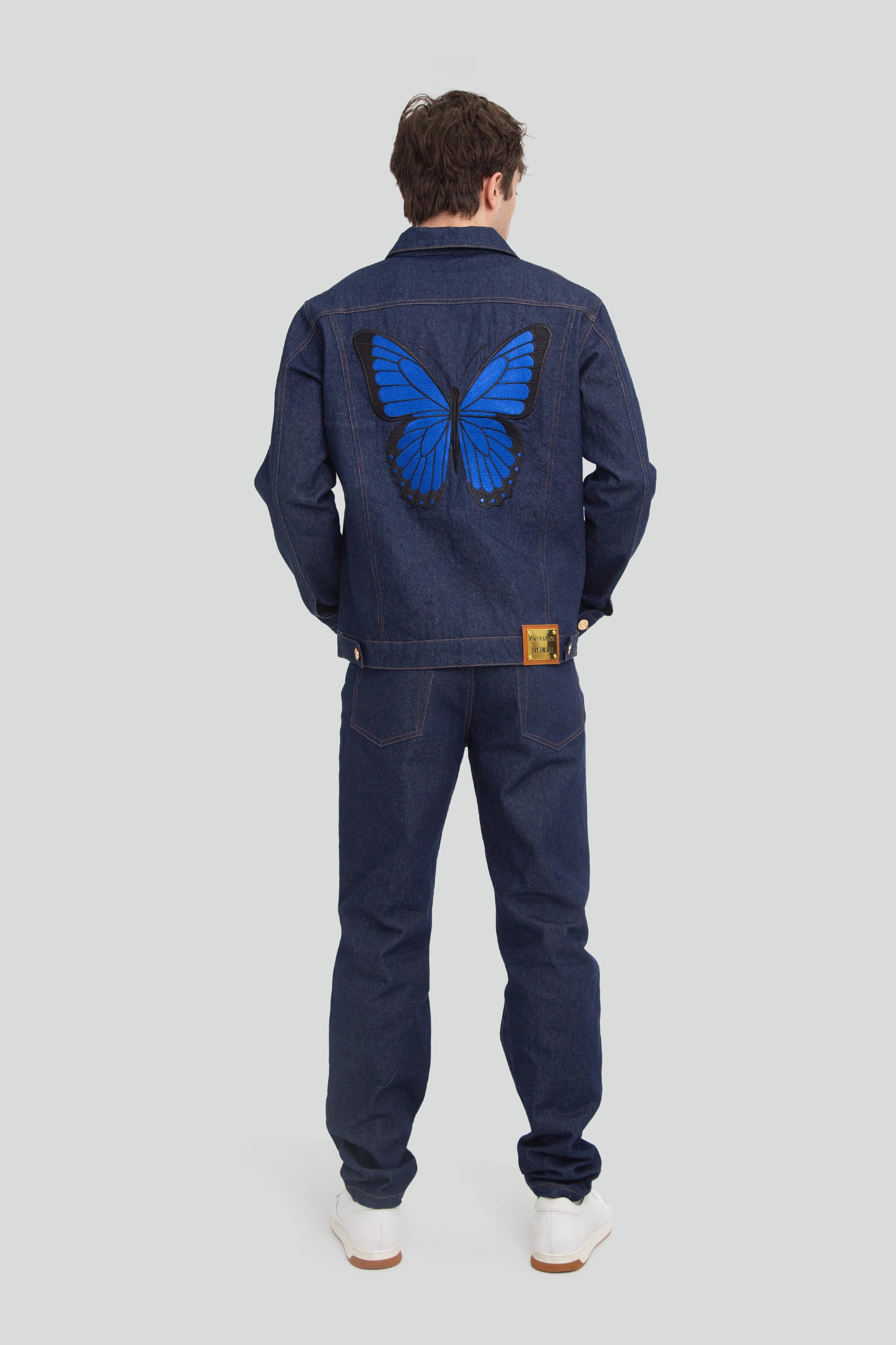 Person wearing a denim outfit with a blue butterfly design on the back, standing against a plain background.