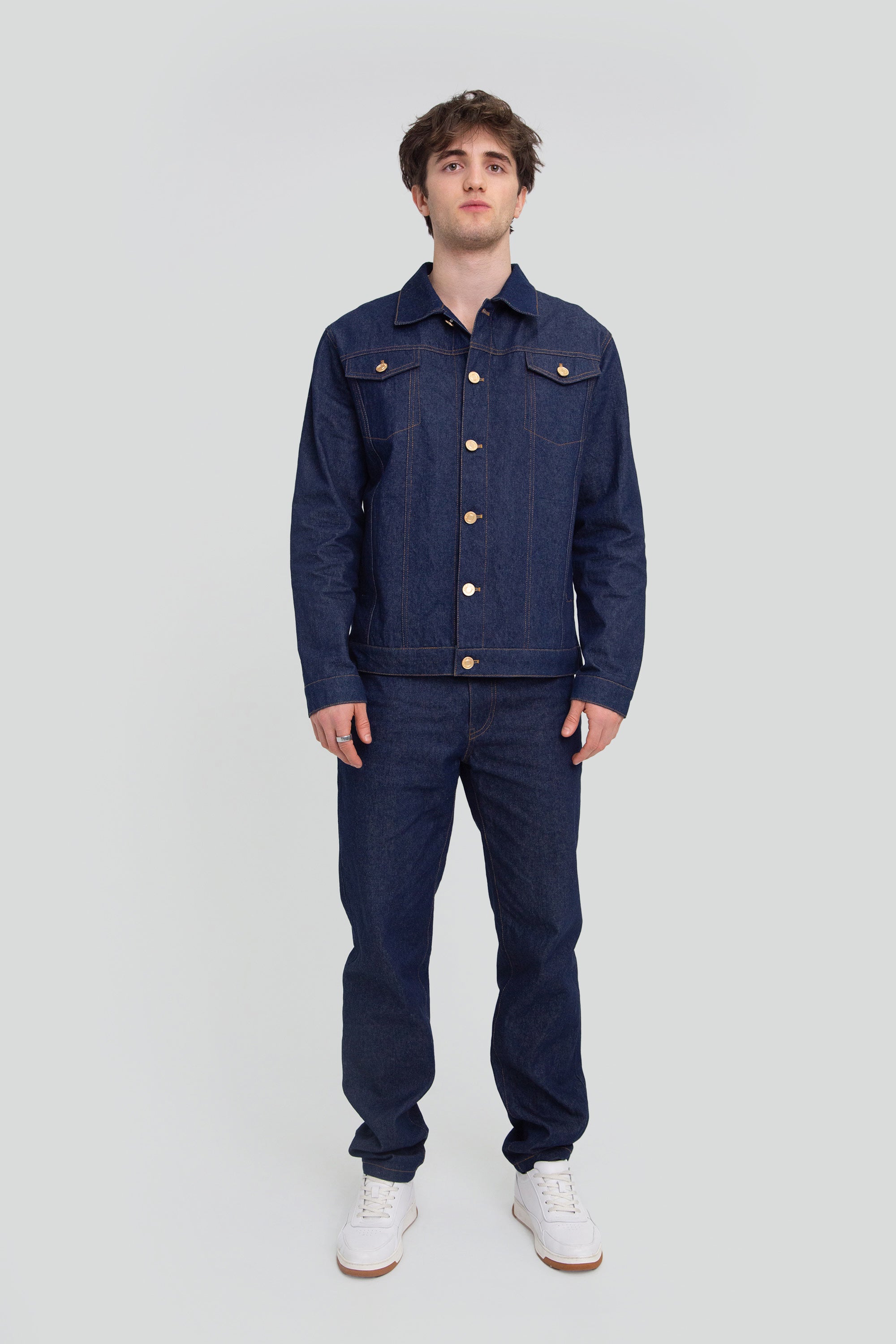 Person wearing a blue denim jacket and pants on a plain background