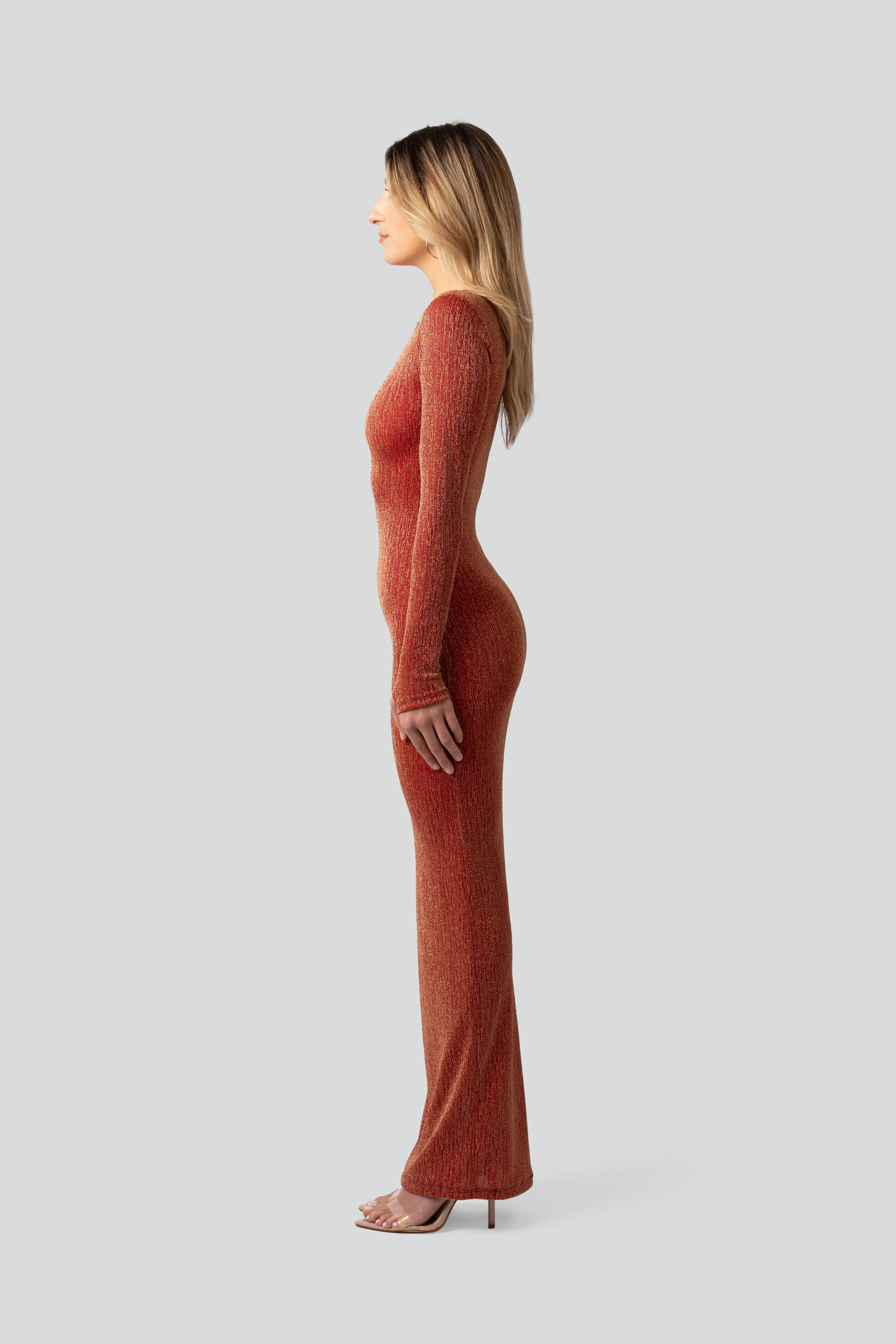Side view of a woman wearing a long-sleeved burnt orange dress against a plain background