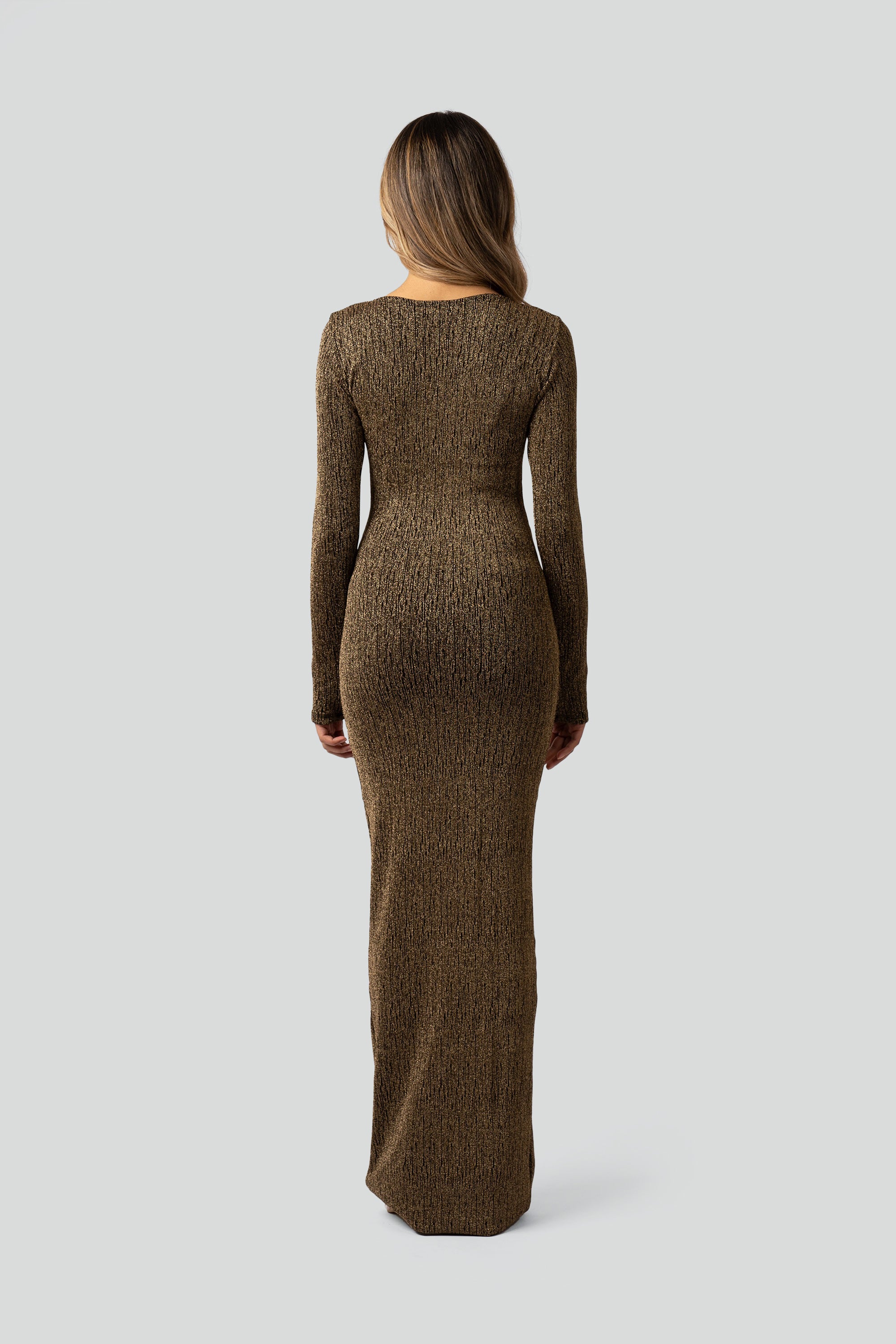 Back view of a woman wearing a gold long-sleeve dress on a gray background