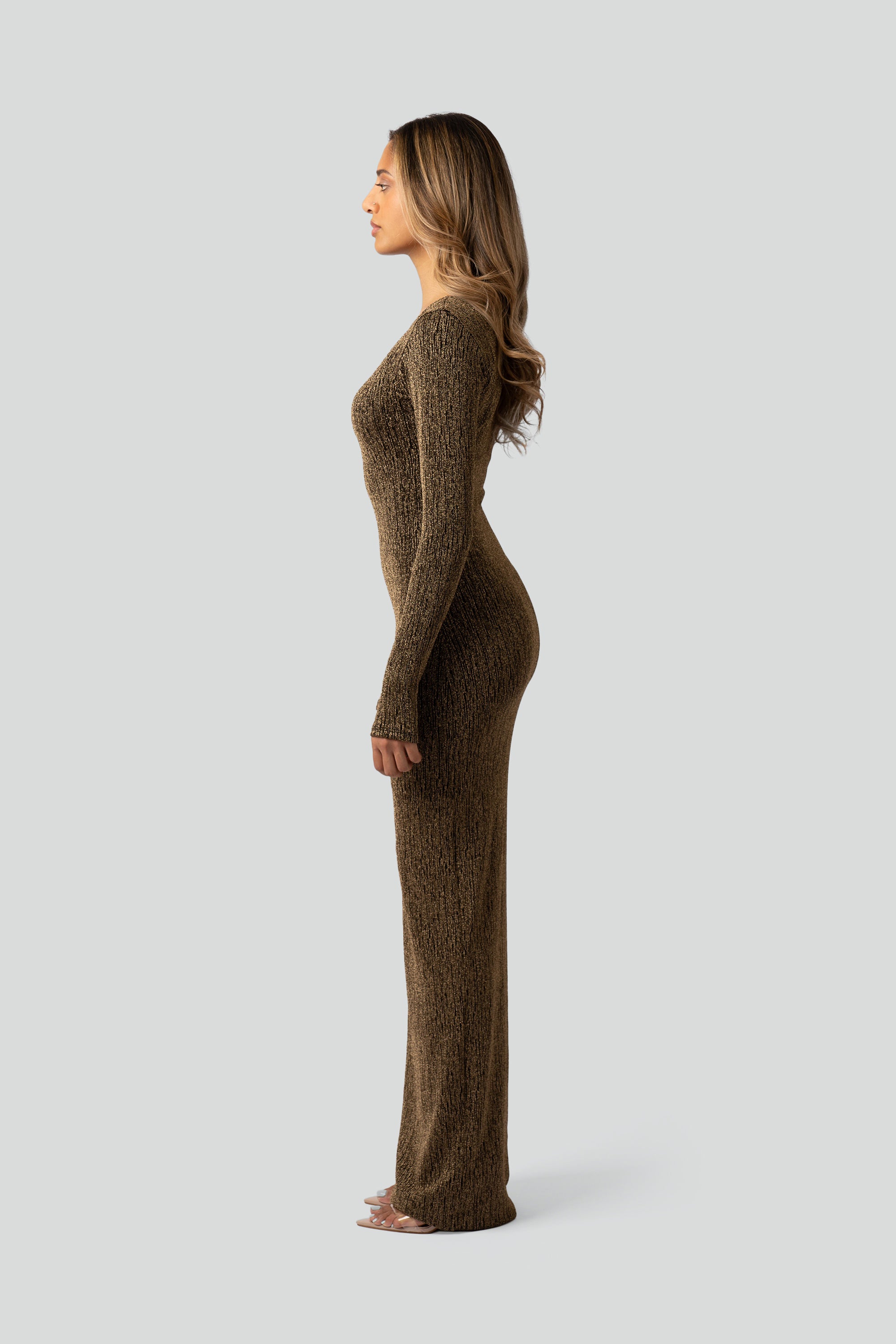 Side view of a woman wearing a gold long-sleeve dress on a gray background