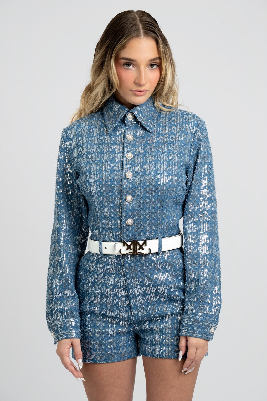 Woman wearing a blue sequin outfit with a white belt on a gray background