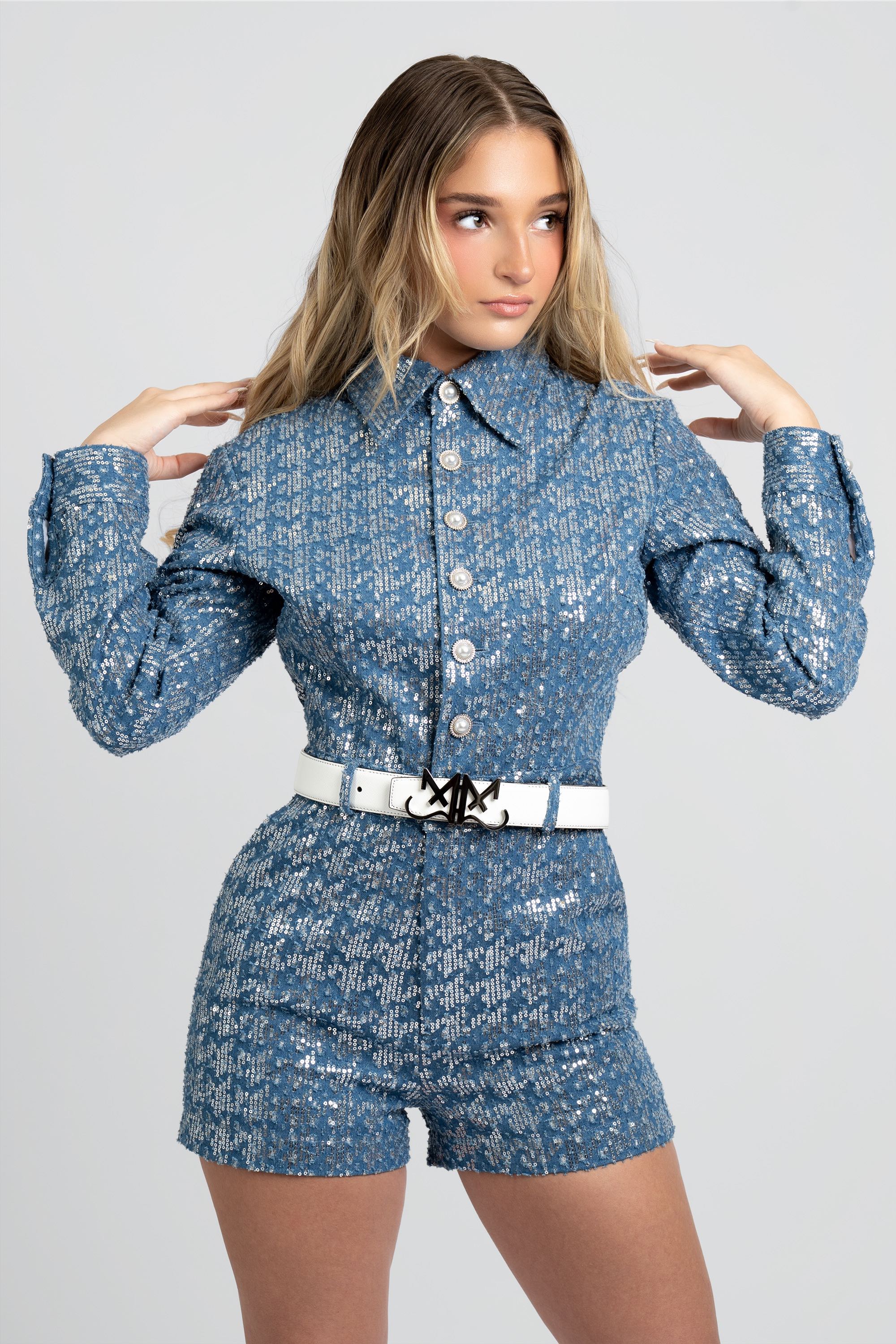 Woman wearing a blue sequin romper with a white belt on a gray background
