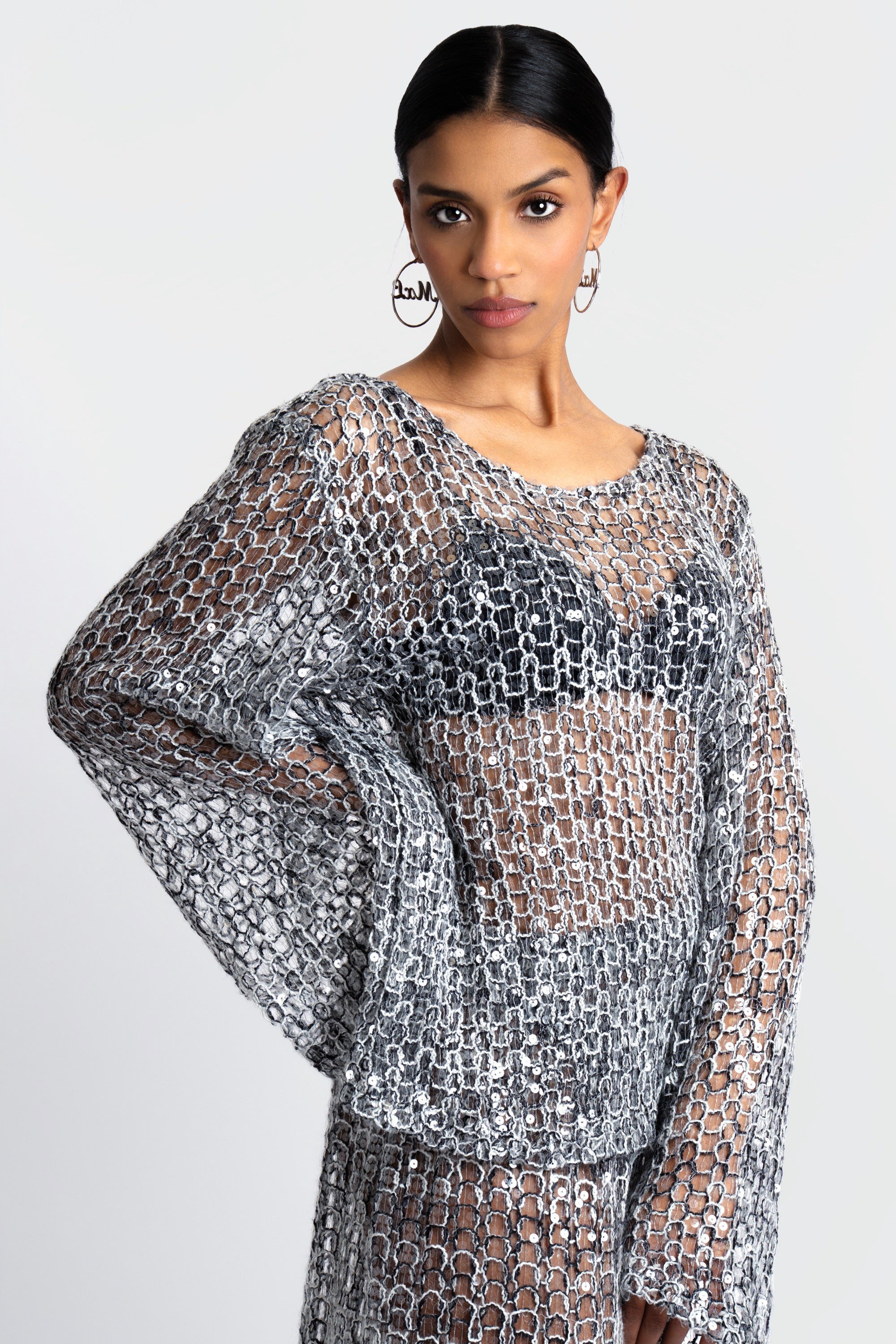 Woman wearing a loose knit top and skirt set with sequins throughout on a white background