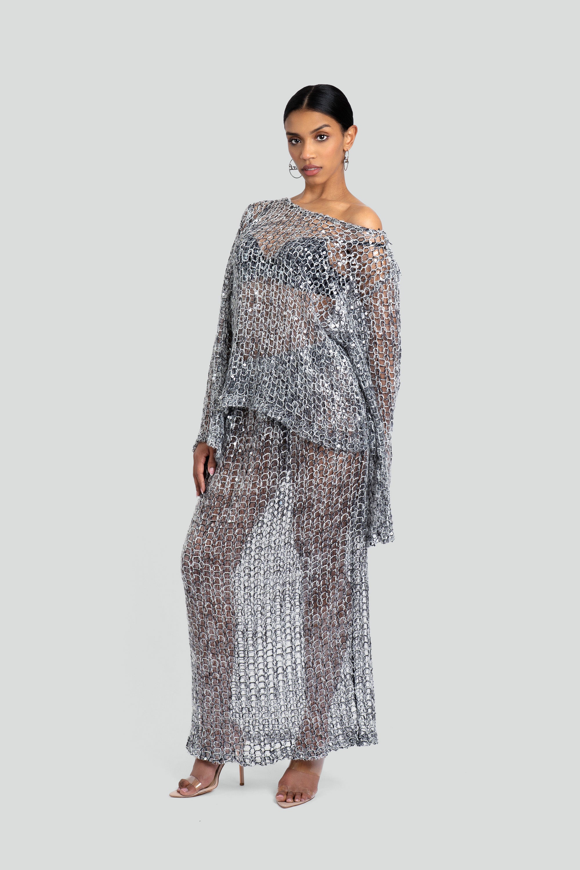 Woman wearing a loose knit top and skirt set with sequins throughout on a white background