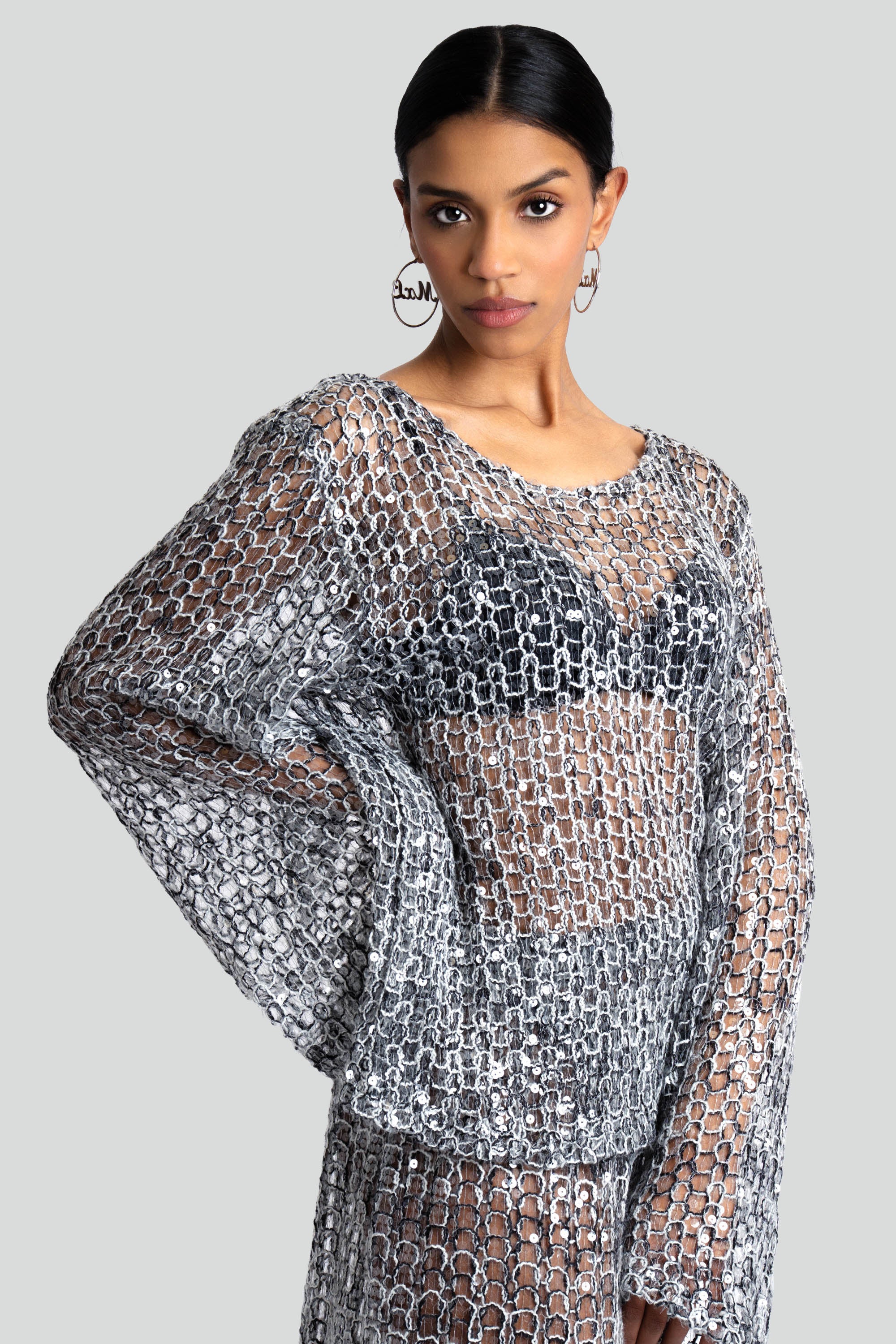 Woman wearing a loose knit top and skirt set with sequins throughout on a white background