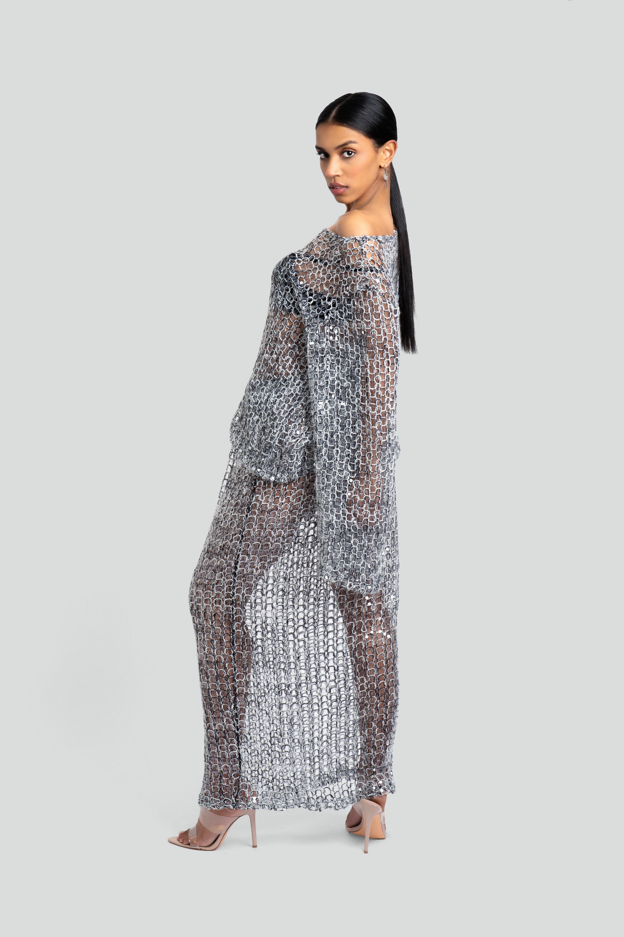 Woman wearing a loose knit top and skirt set with sequins throughout posing against a white background