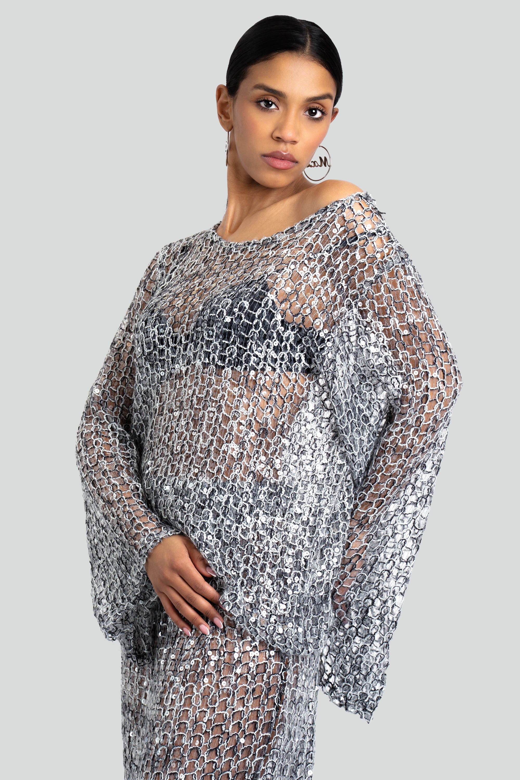 Woman wearing a loose knit top and skirt set with sequins throughout posing against a white background