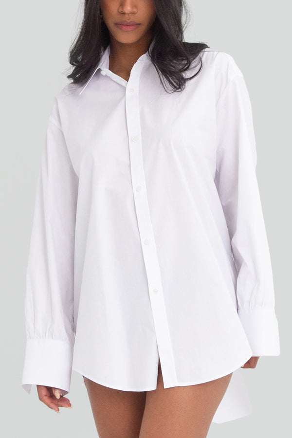 White oversized button up shirt worn as a mini dress, featuring a structured natural fiber fabric, crisp spread collar, and long cuffed sleeves
