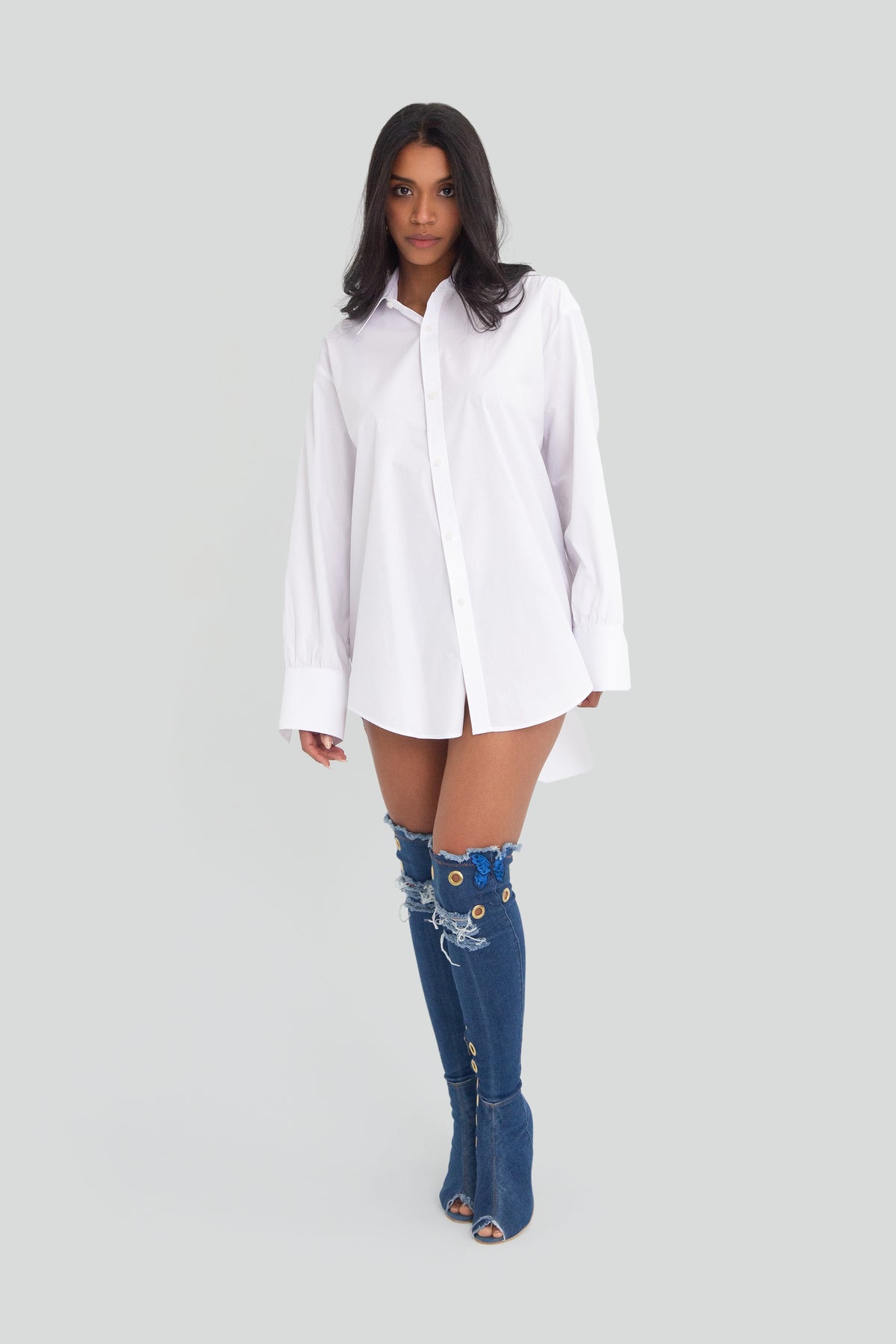 White oversized button up shirt worn as a mini dress, featuring a structured natural fiber fabric, crisp spread collar, and long cuffed sleeves