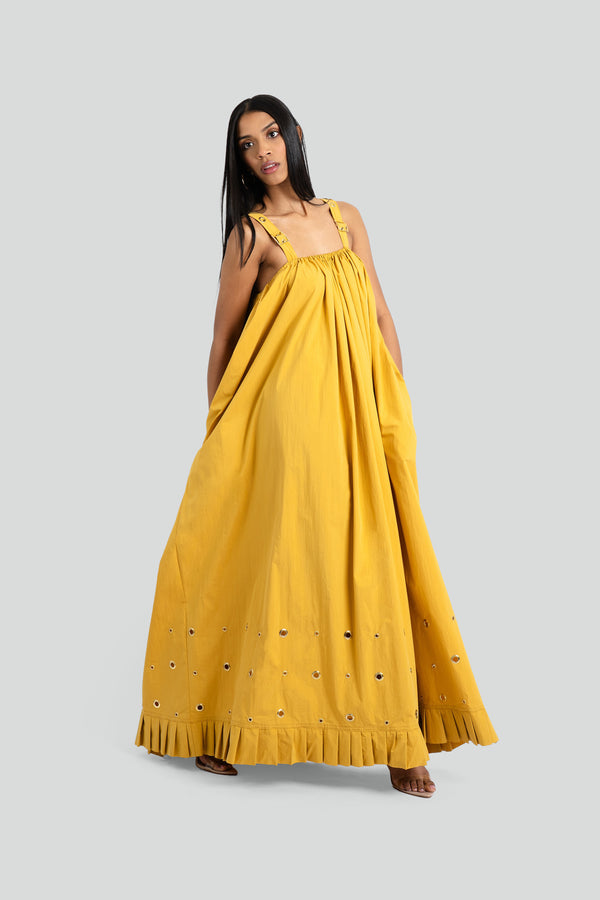  Floor-length bohemian maxi dress in a soft mustard yellow fabric, featuring a gathered neckline, wide structured straps, and a pleated hem