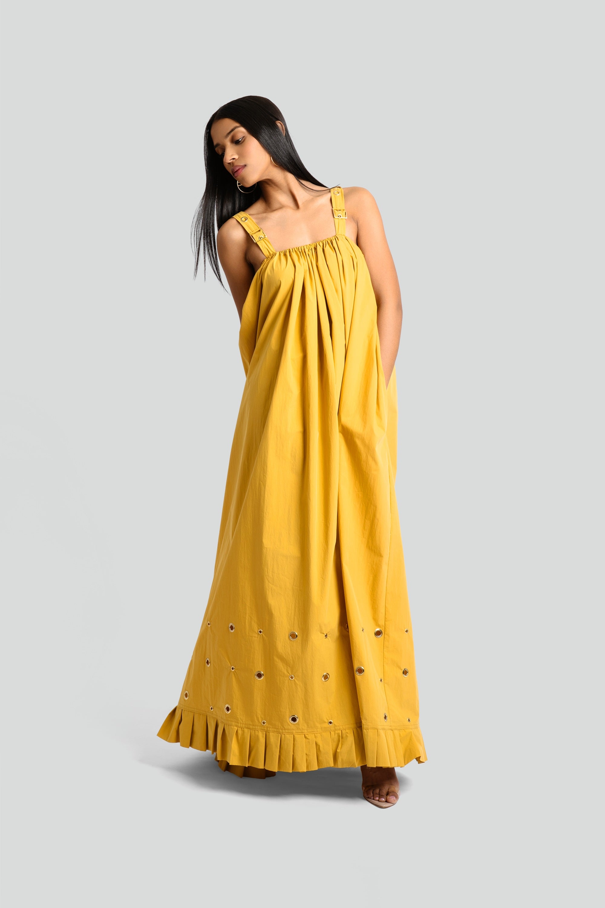 Model styling a mustard yellow maxi dress with structured grommet straps from the Maui X Lolita collection