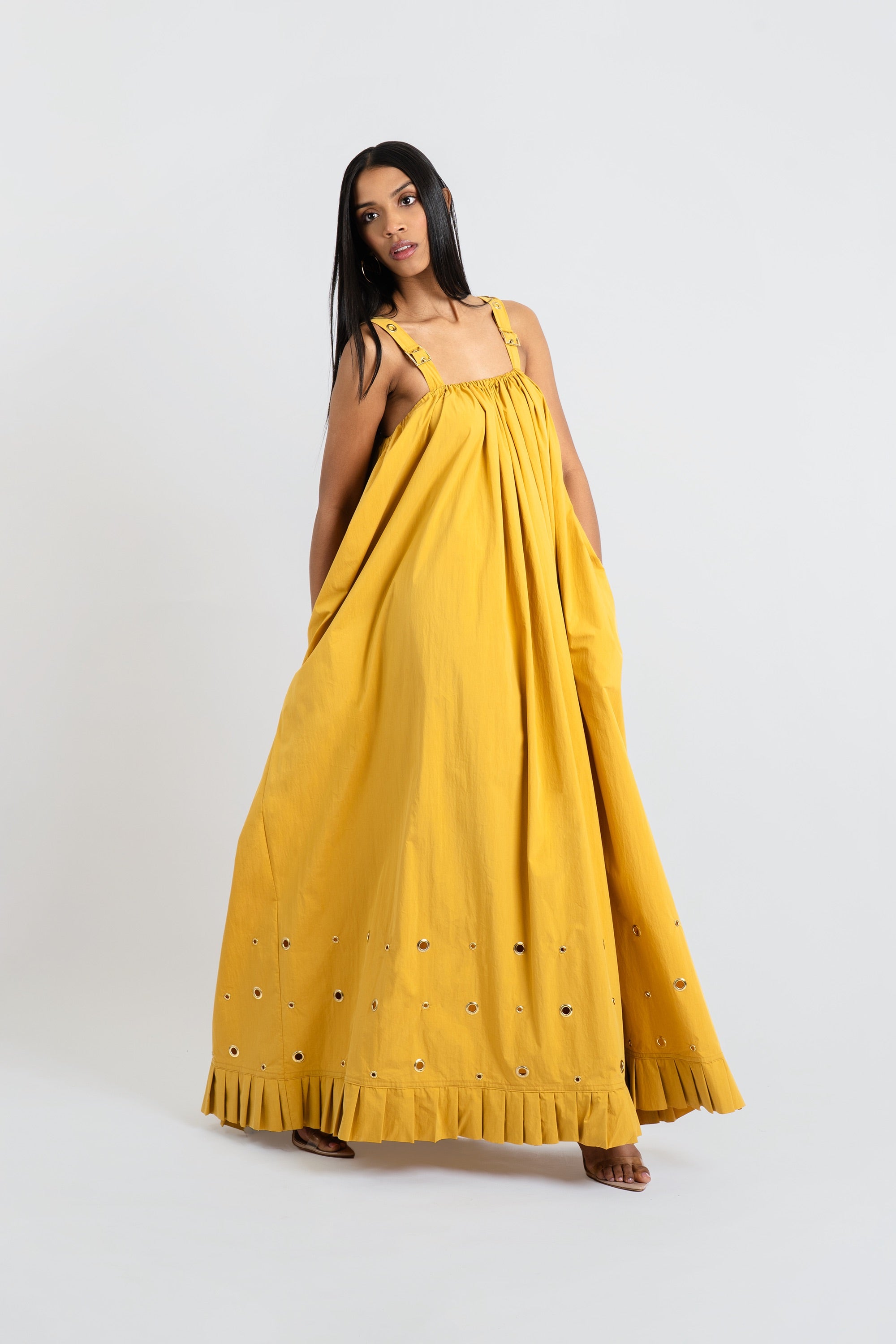 Woman wearing a yellow dress with grommet detailing on a white background