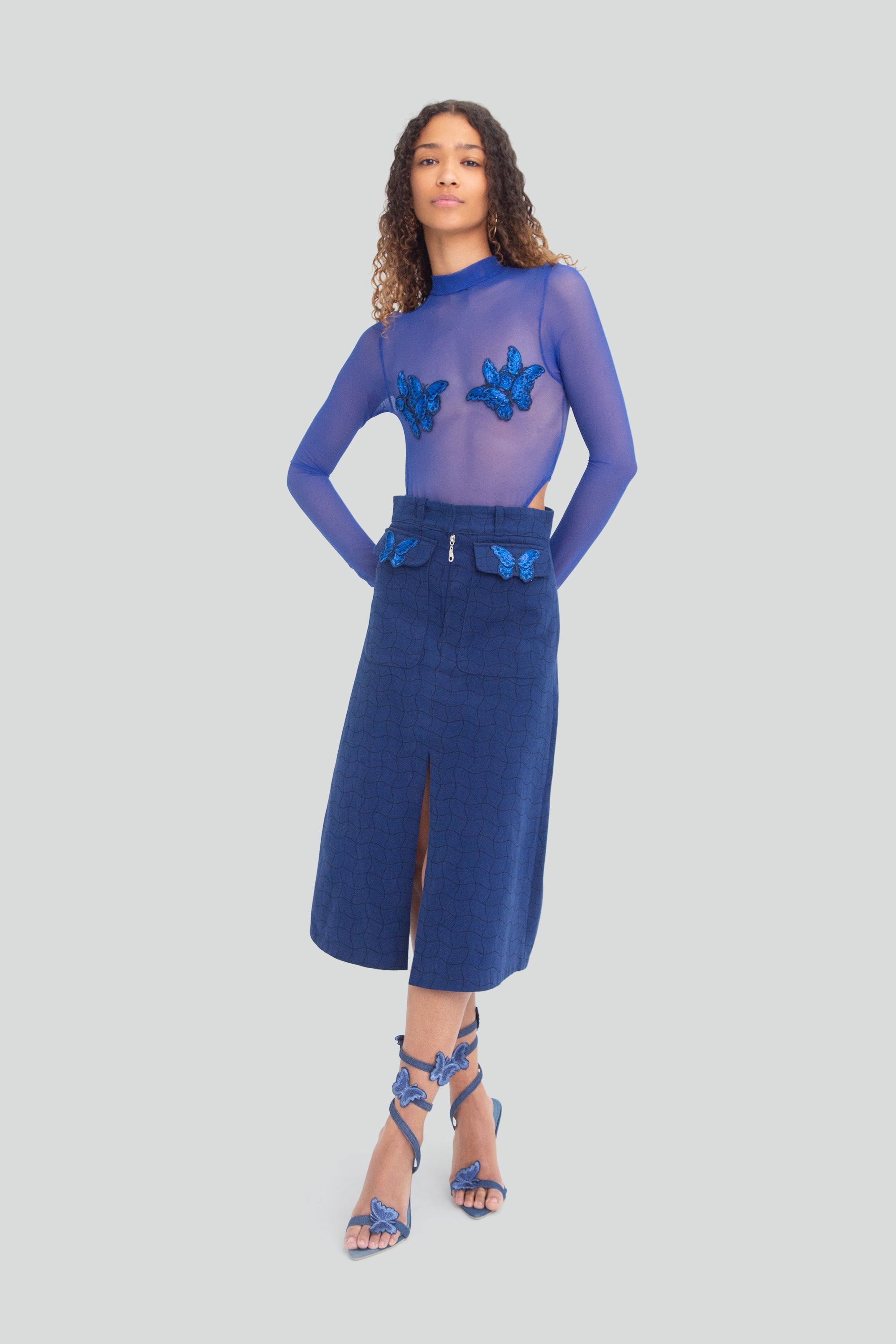 Woman wearing a blue outfit with butterfly details on a plain background