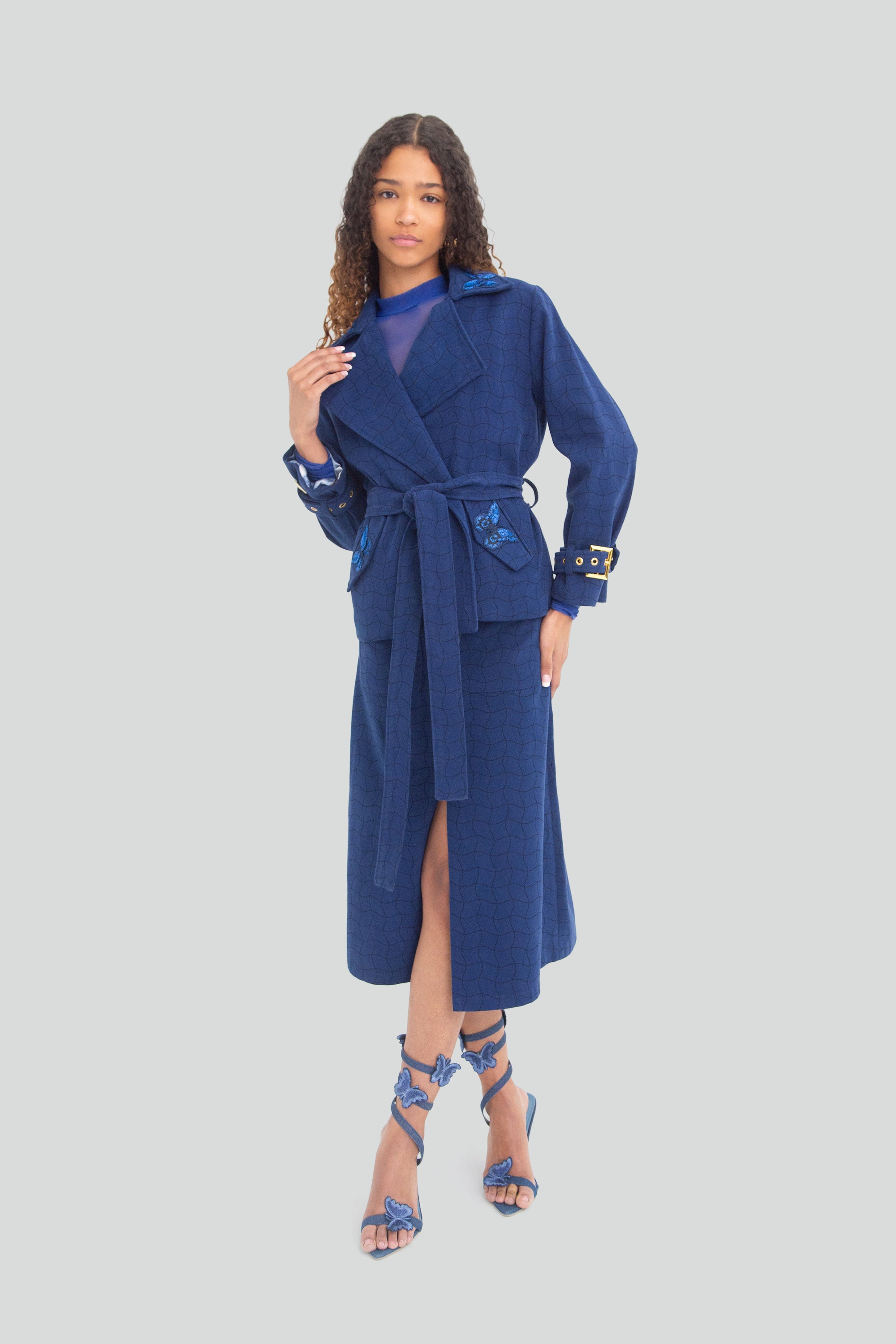 Woman wearing a blue coat with butterfly details and skirt on a plain background