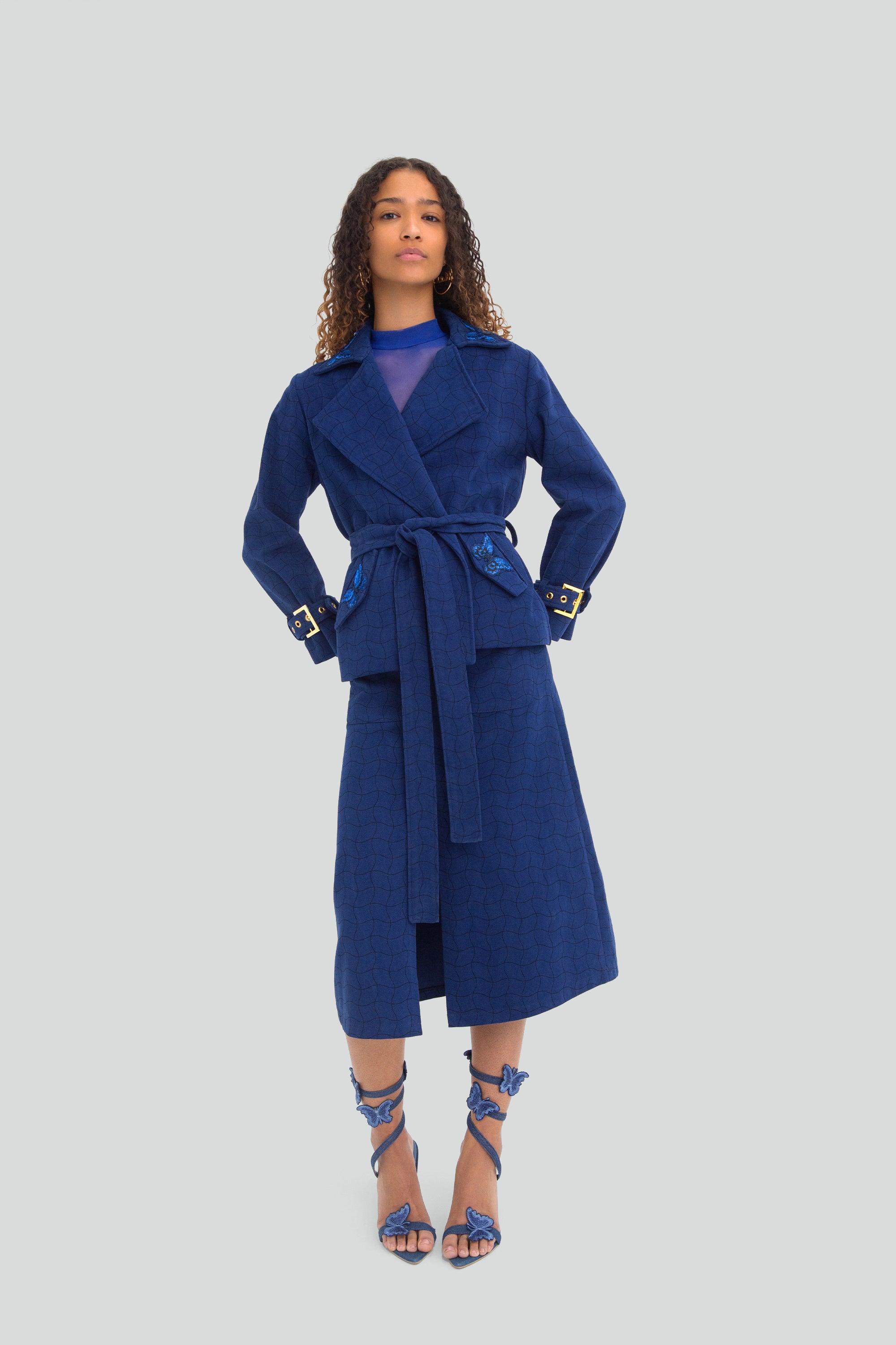 Woman wearing a blue coat and skirt set on a light gray background