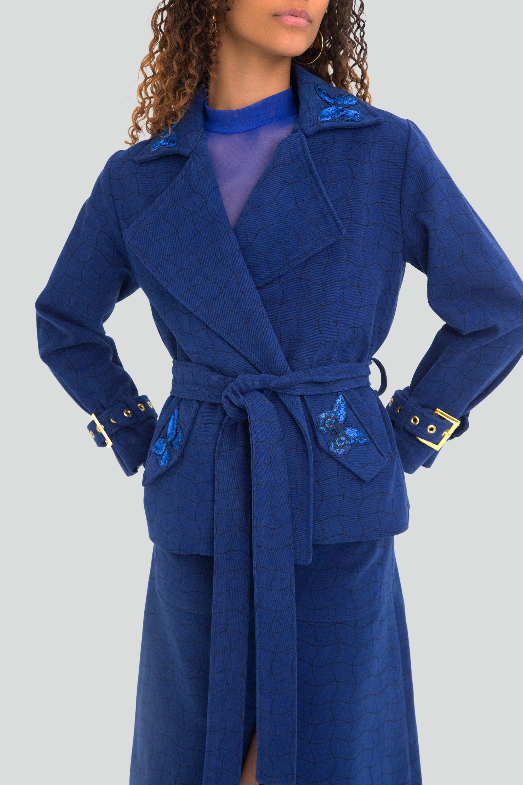 Woman wearing a blue coat with butterfly embroidery on a light gray background