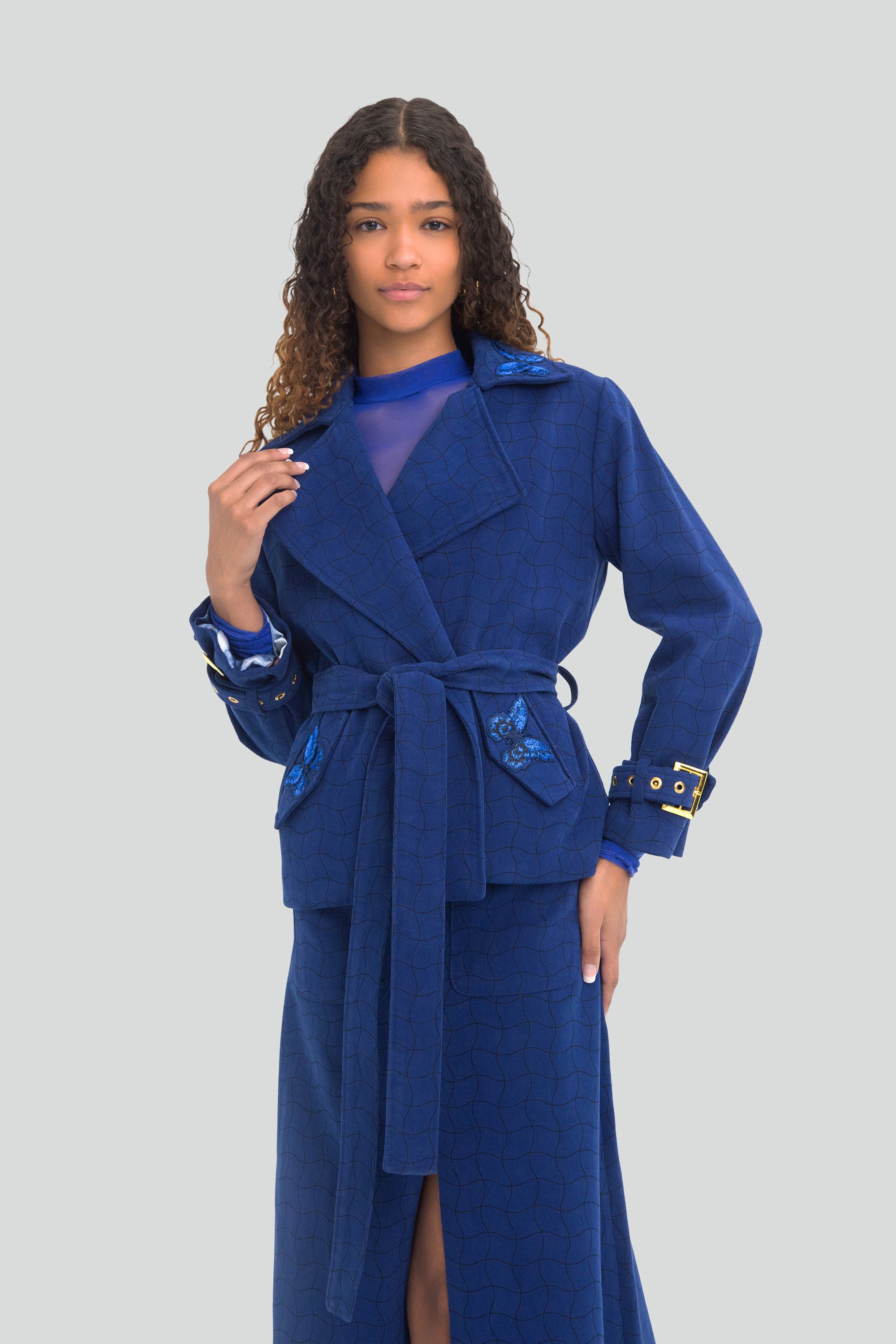 Woman wearing a blue coat and skirt set with a light gray background