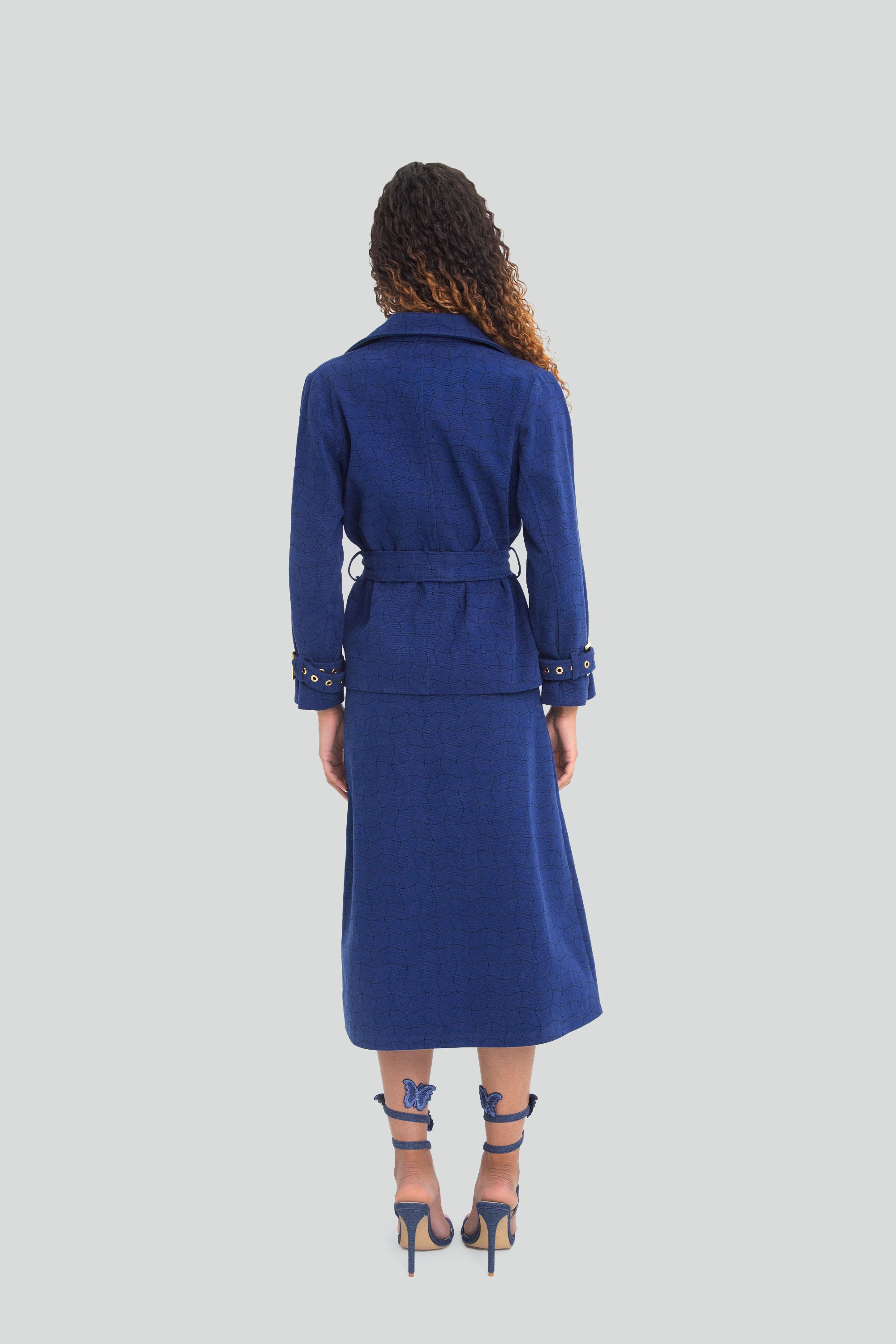 Woman wearing a blue coat and skirt set on a light gray background