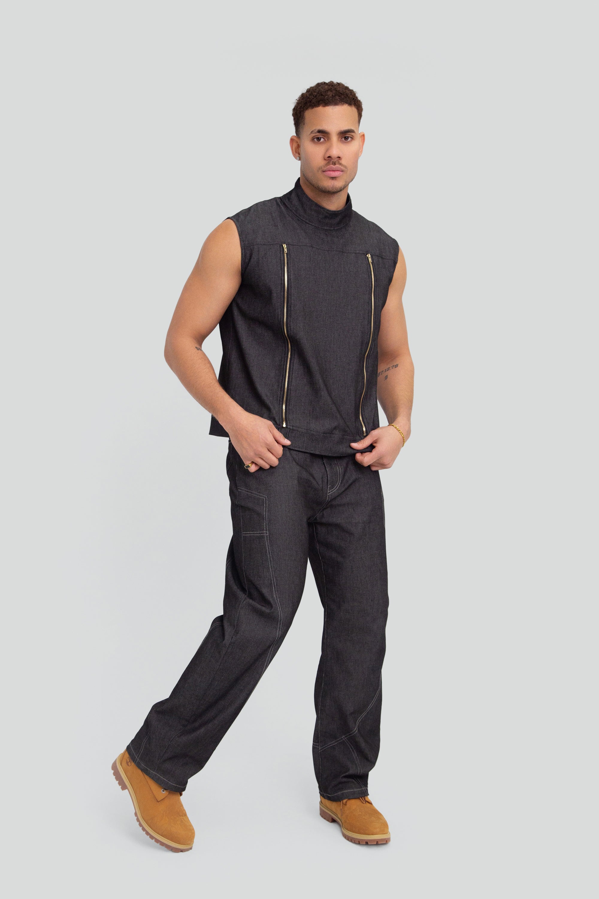 Man wearing a grey denim mock neck vest and matching pants on a plain background