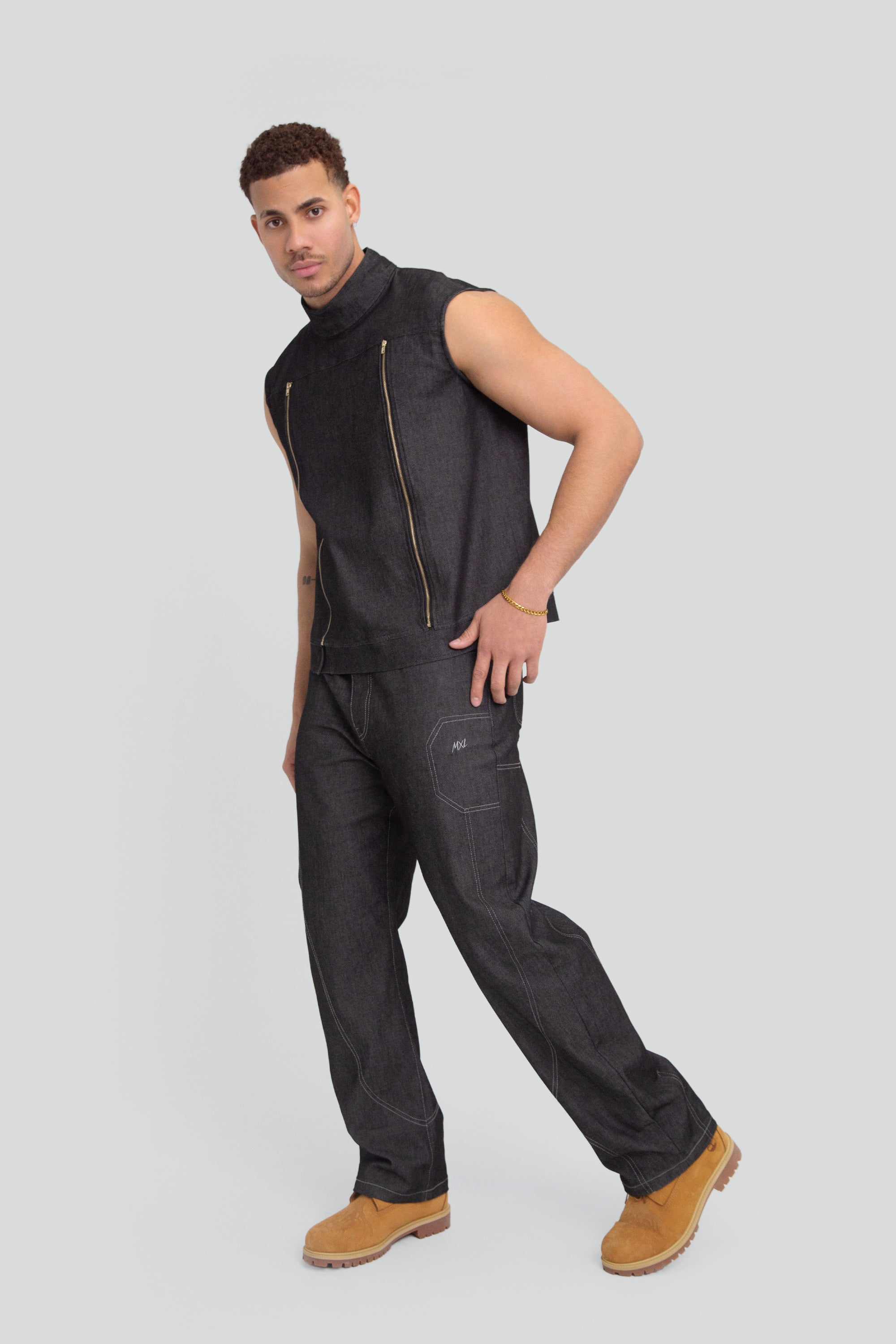Man wearing a grey denim mock neck vest and matching pants on a plain background
