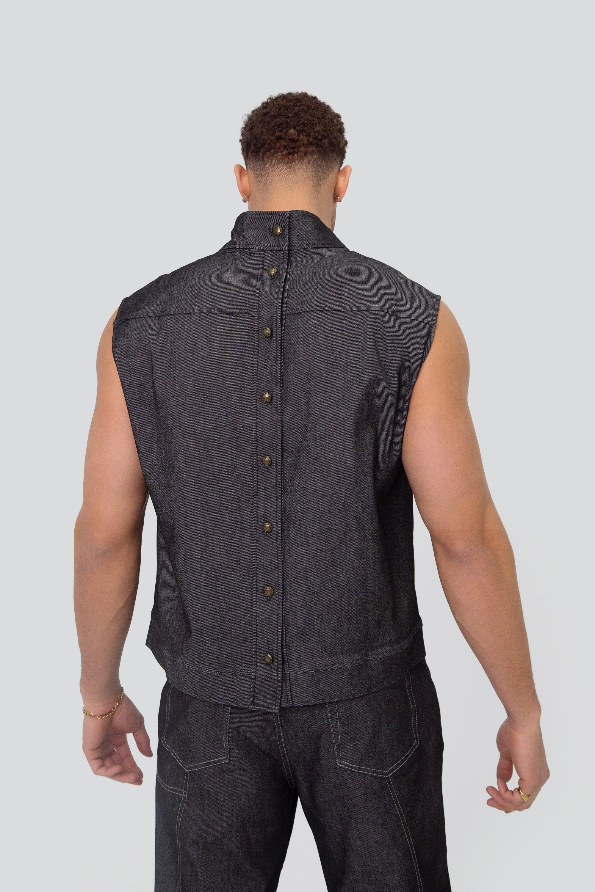 Man wearing a grey denim mock neck vest and matching pants on a plain background