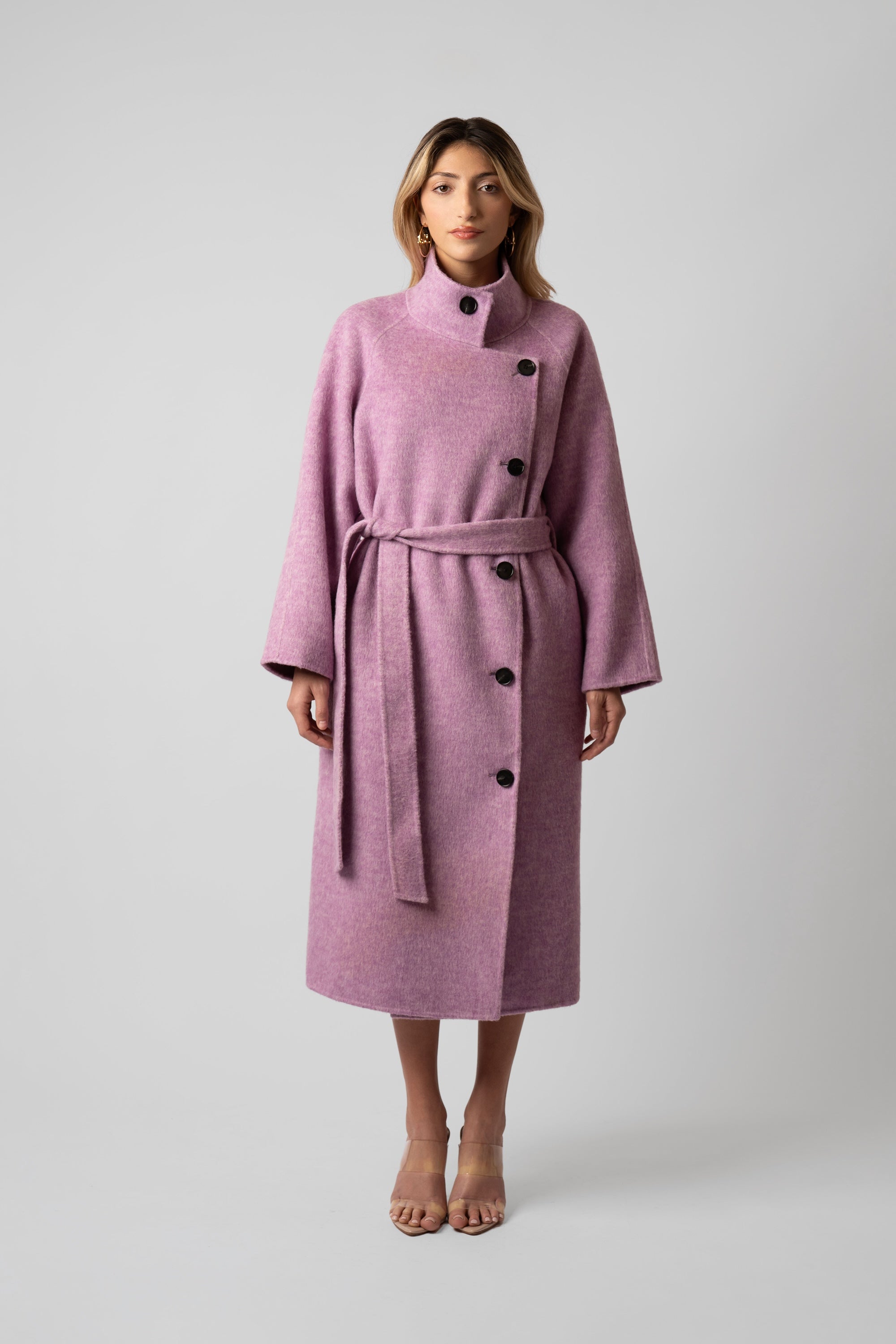 Woman wearing a pink wool coat with buttons and belt on a white background