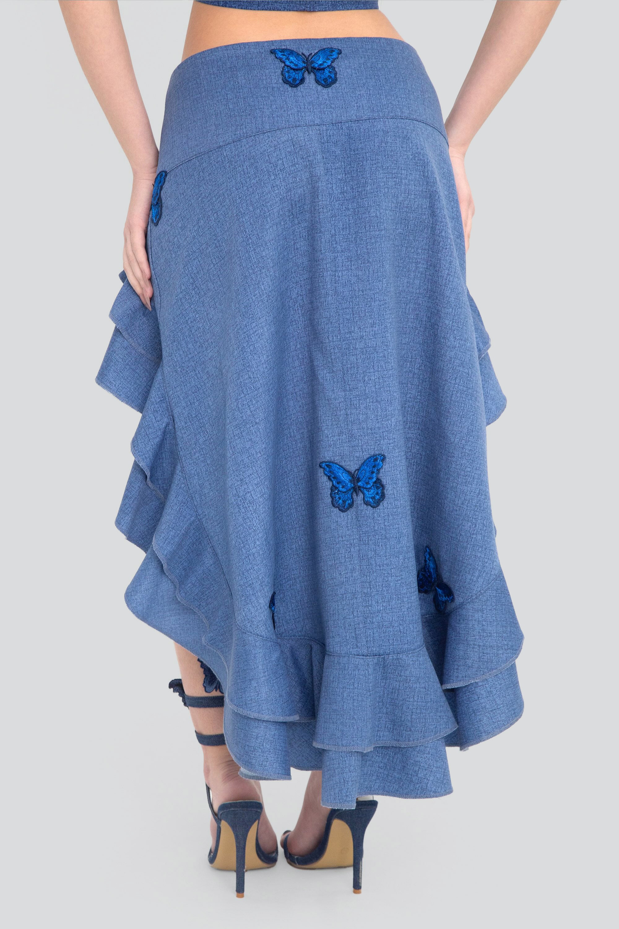 Blue denim high-low skirt with ruffles and butterfly details on a plain background