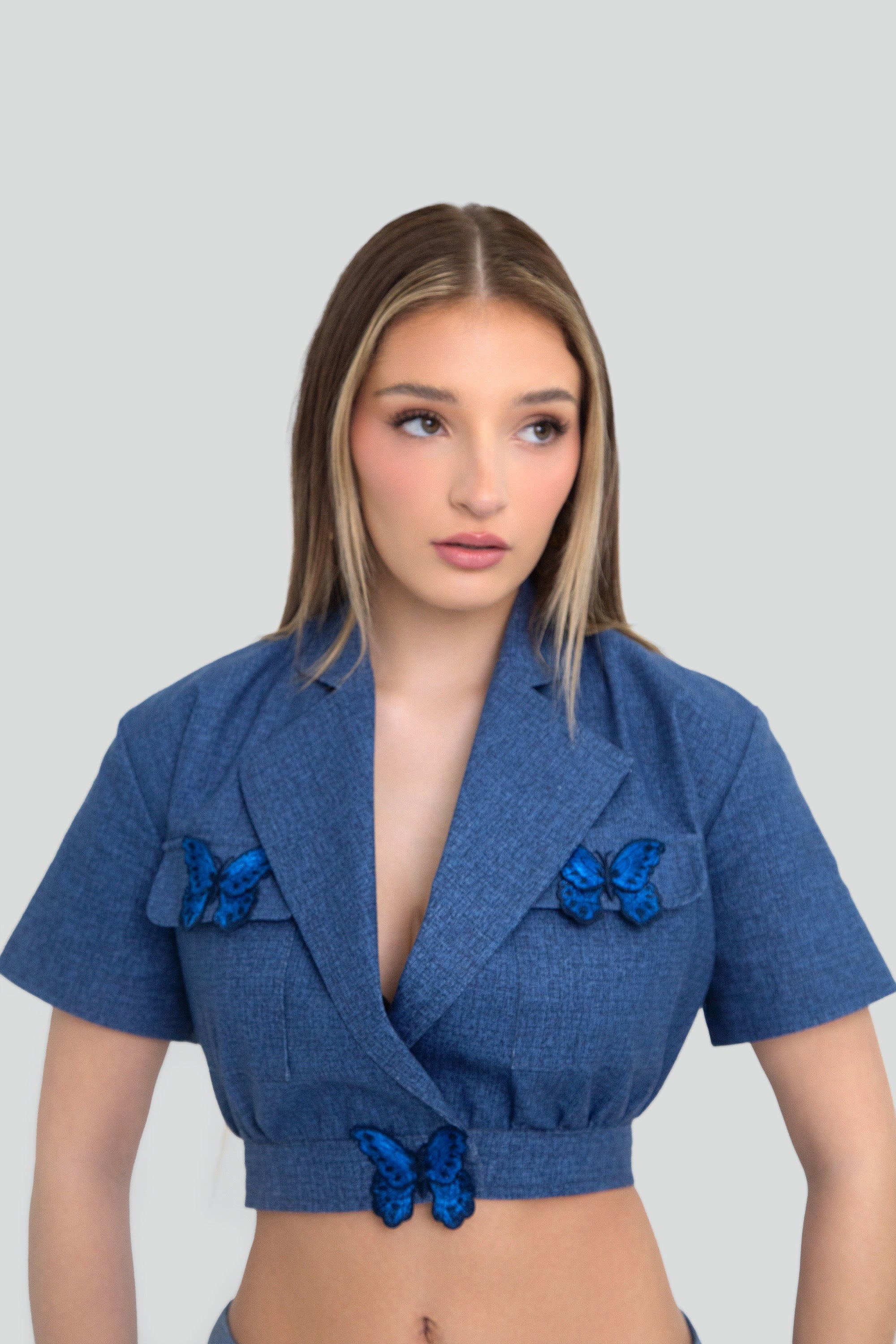 Woman wearing a blue top with butterfly details on a plain background