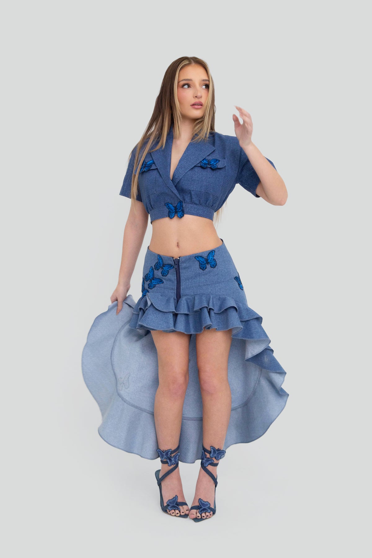 Woman wearing a blue medium wash denim matching set featuring a boxy cropped top with puff sleeves and a ruffled high low skirt