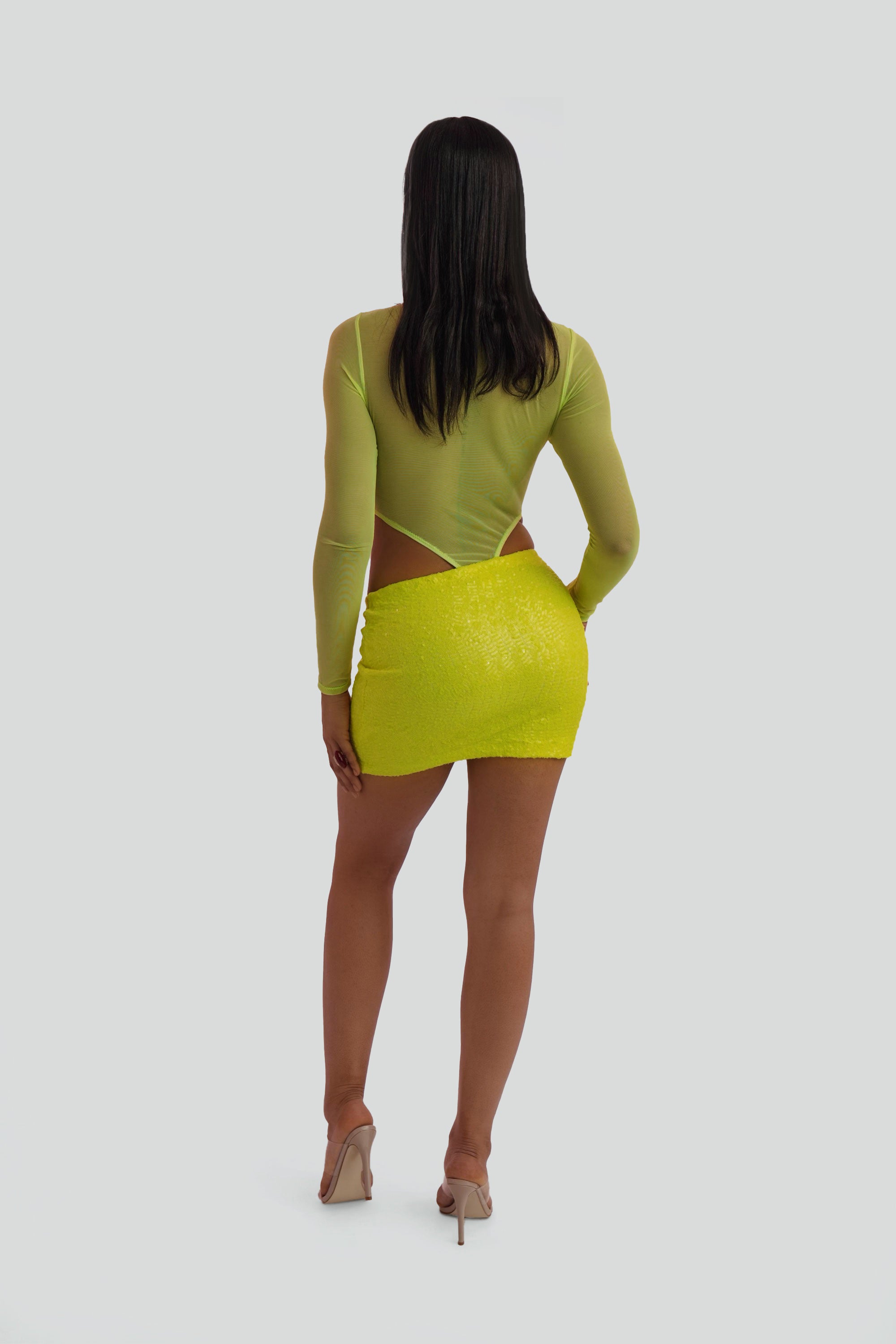 Woman wearing a neon yellow sequin mini skirt and sheer top on a white background
