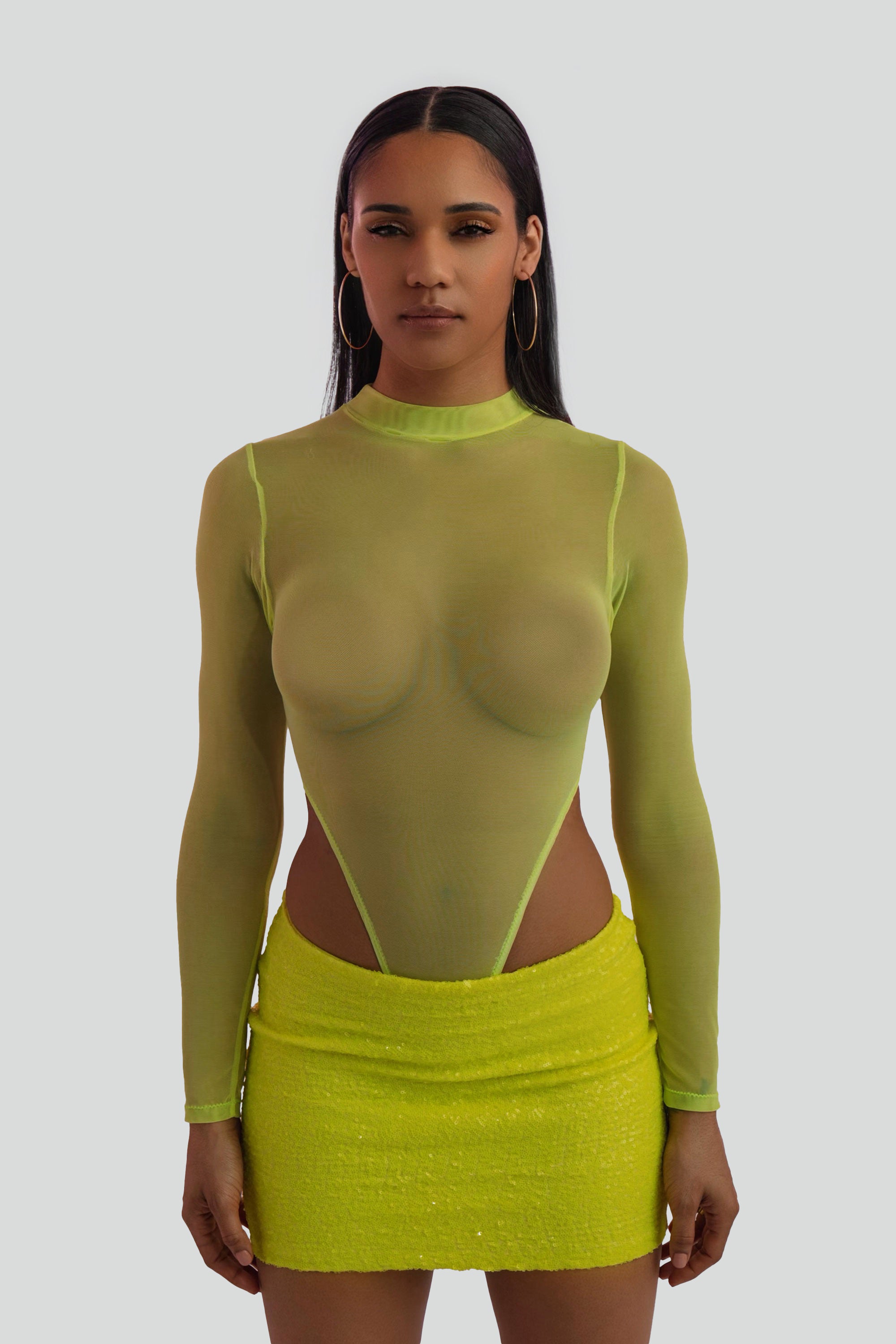 Woman wearing a neon yellow sequin mini skirt and sheer top on a white background