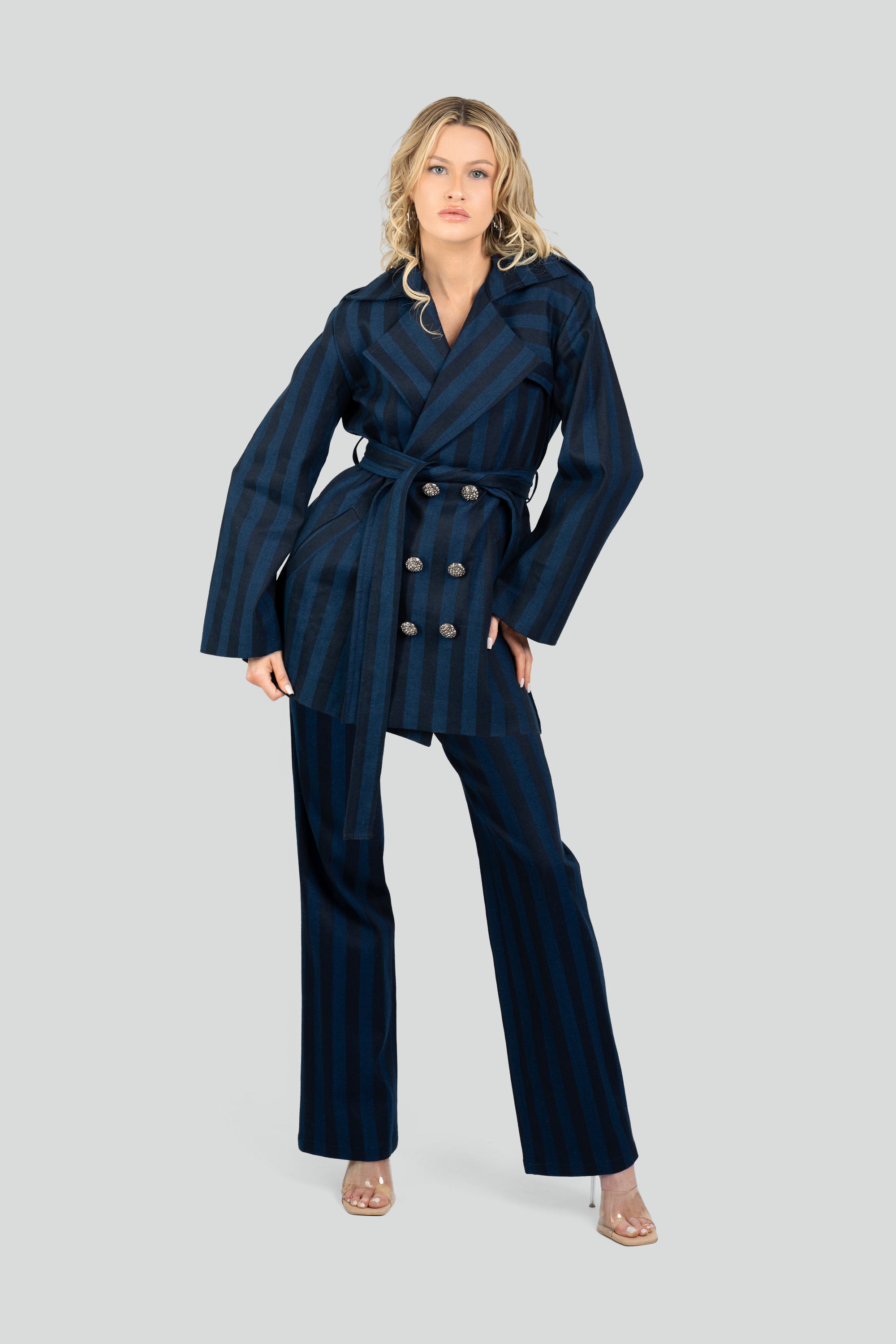 Woman wearing a navy striped short trench coat and tied waist belt with matching pants on a white background