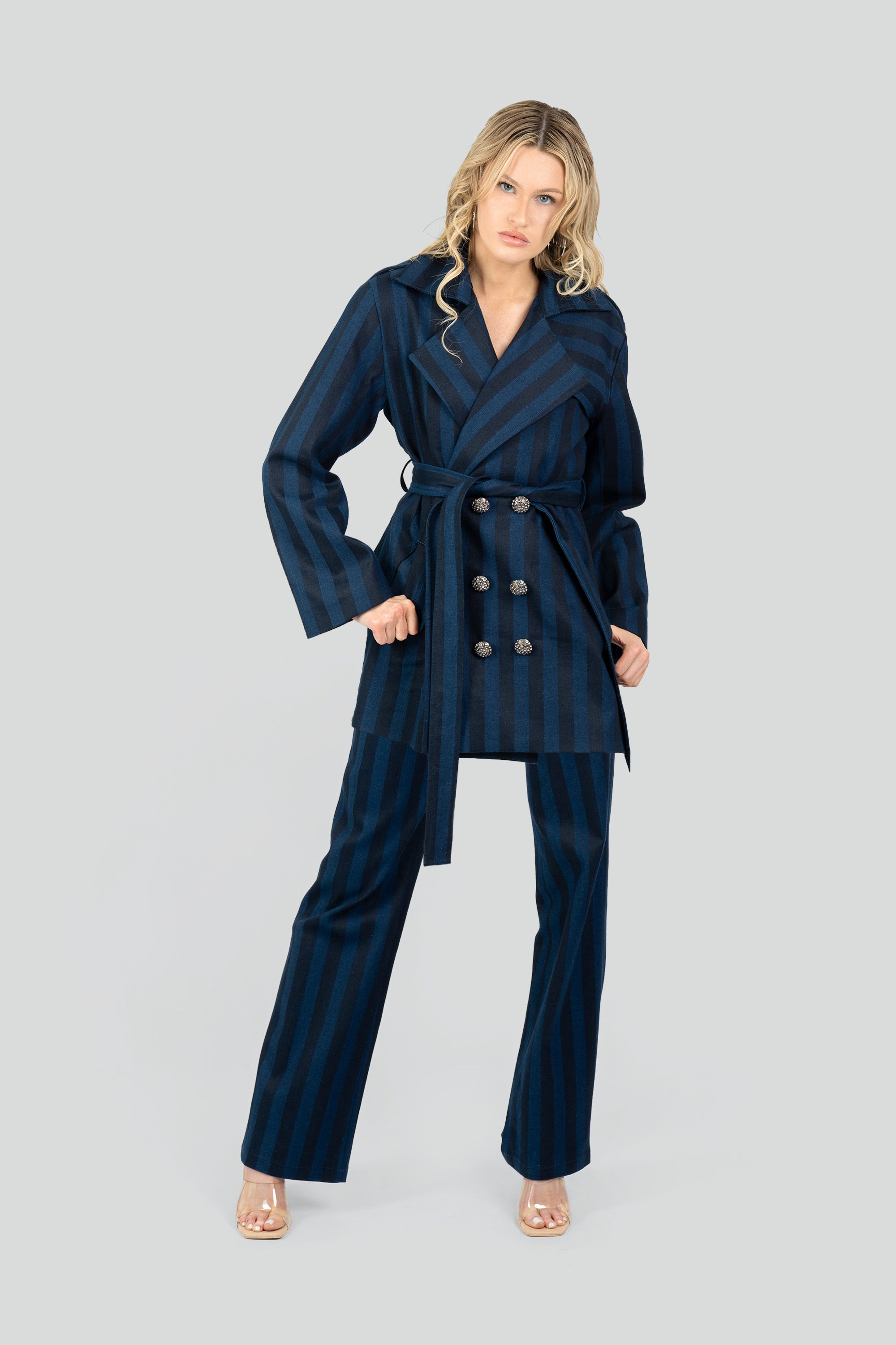 Woman wearing a navy striped short trench coat and tied waist belt with matching pants on a white background