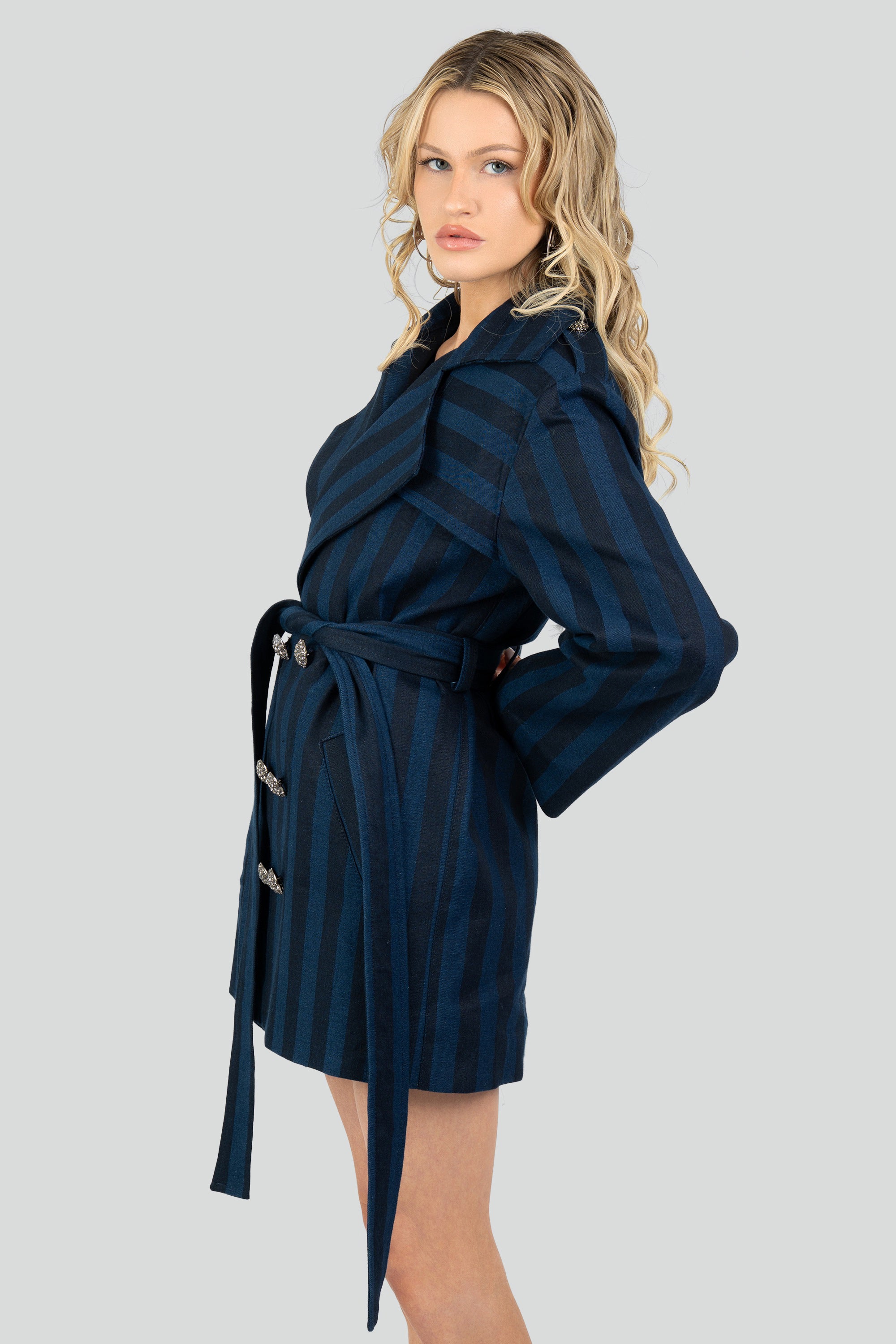 Woman wearing a navy striped short trench coat and tied waist belt on a white background