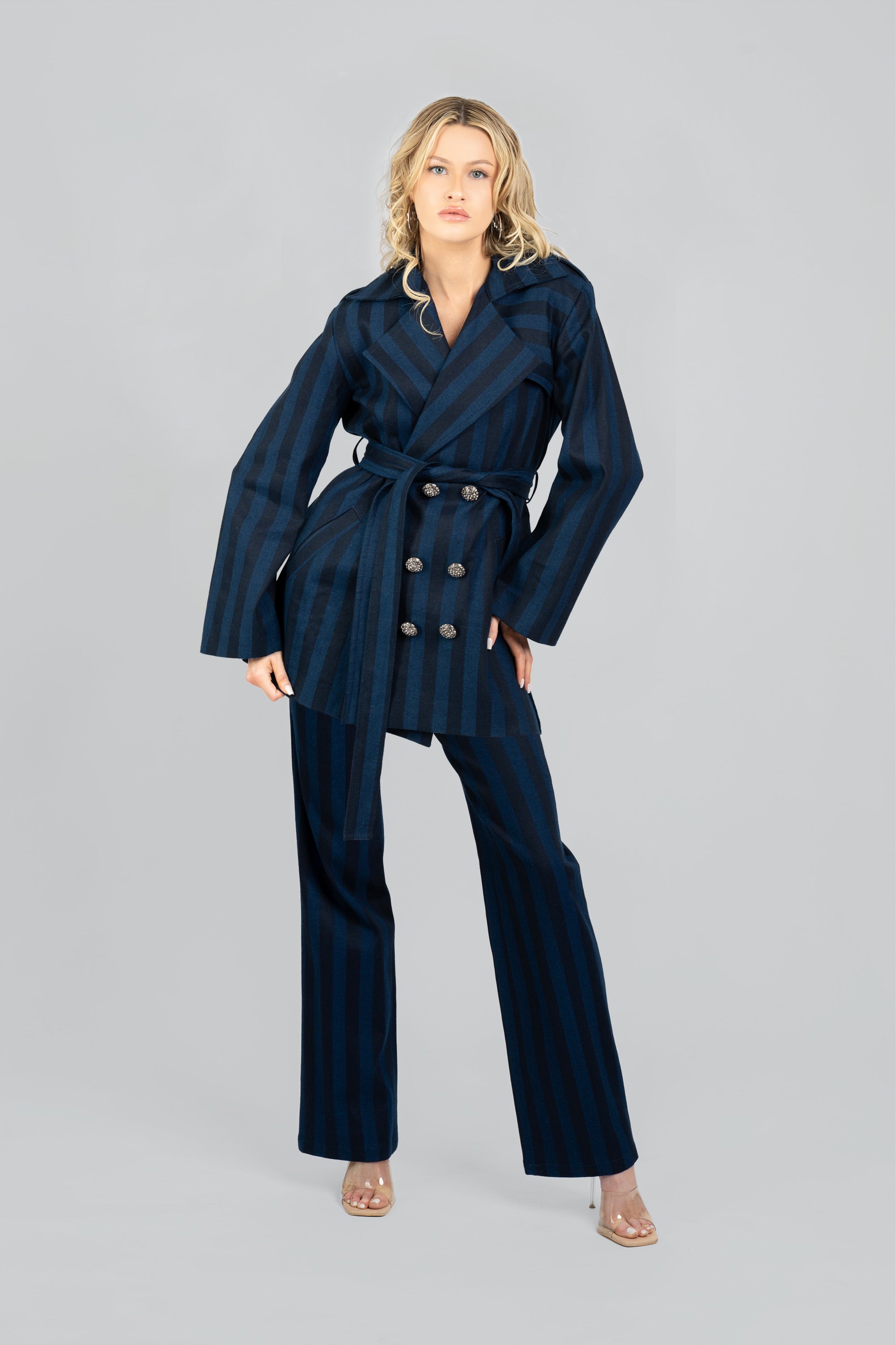 Woman wearing a navy striped short trench coat and tied waist belt with matching pants on a white background