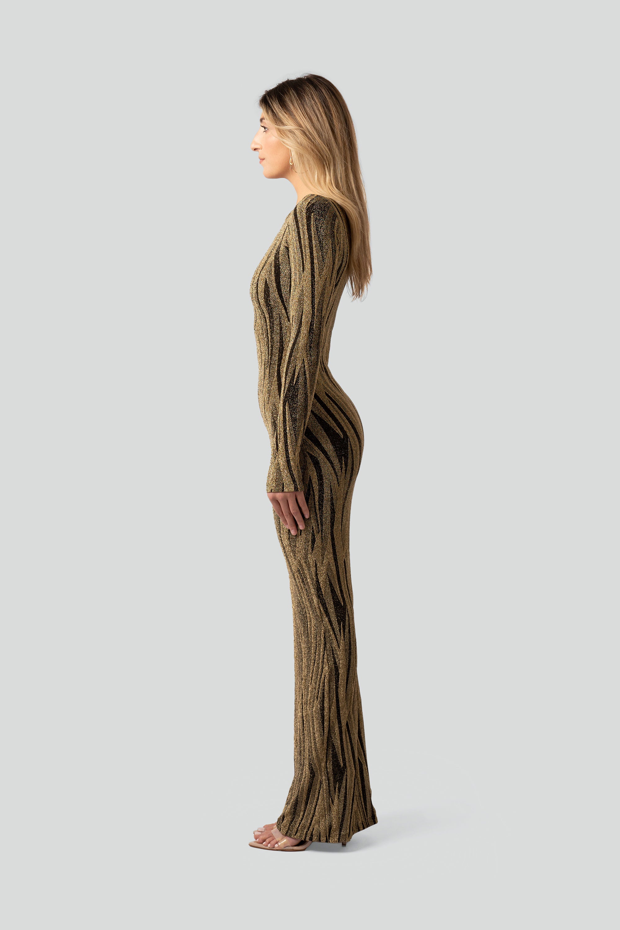 Side view of a woman wearing a gold and black patterned dress on a gray background